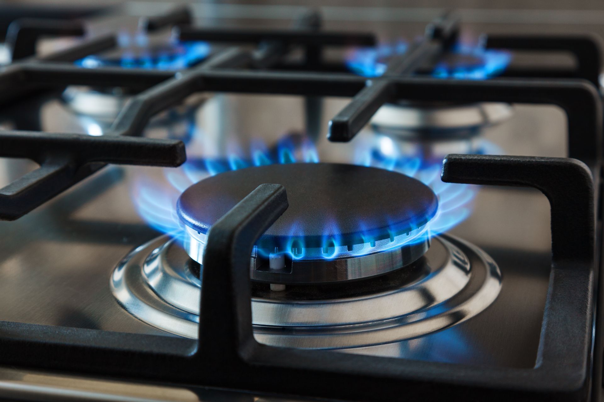 Stainless steel cooktop featuring a cast iron grill and burning gas flames. Stainless steel cooktop featuring a cast iron grill and burning gas flames.