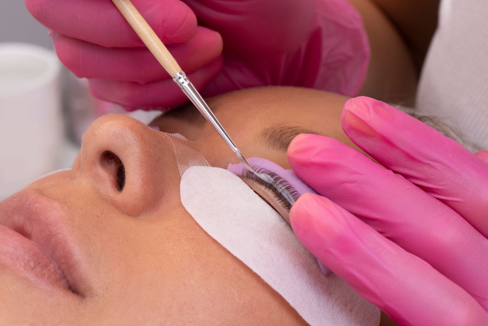 Einer Frau werden die Wimpern von einer Frau mit rosa Handschuhen gemacht.