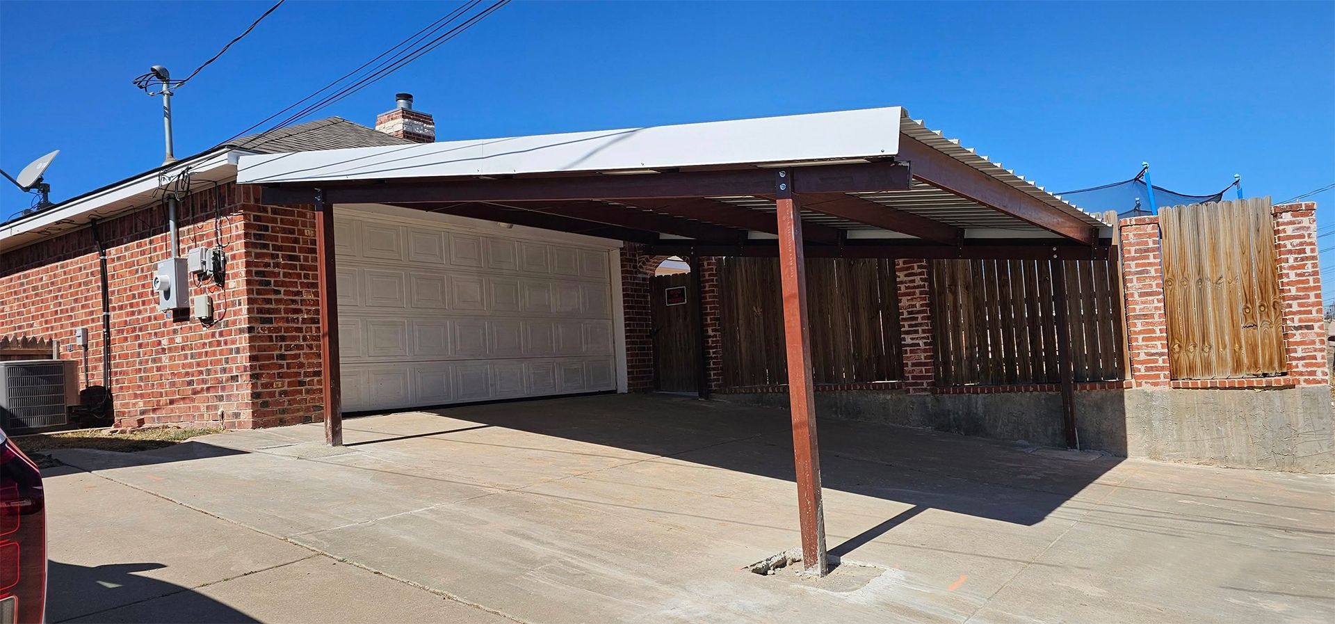 Brick house with a carport, driveway, and wooden fence on a sunny day.