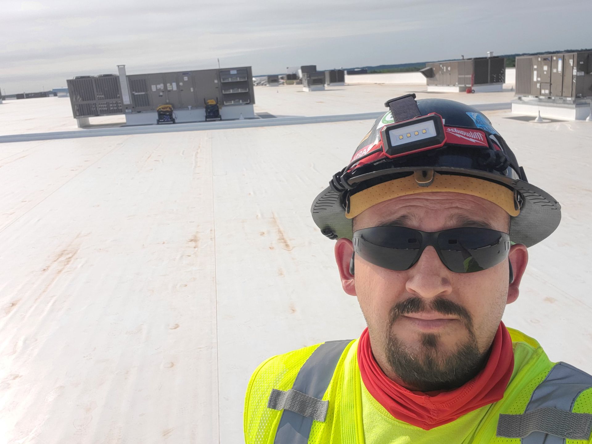 Man in safety gear on a rooftop, wearing sunglasses and a hard hat with a headlamp, looking at the camera.