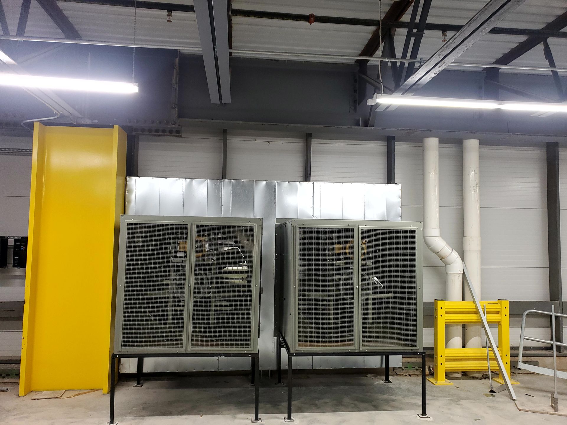 Two electrical cabinets with metal ductwork, and yellow safety barriers, indoors.