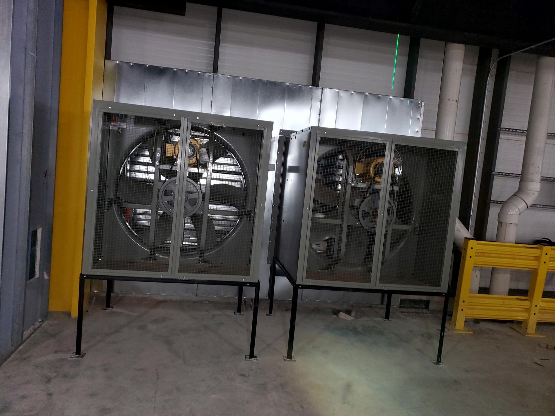 Two large industrial fans with protective cages, set against a metallic backdrop.