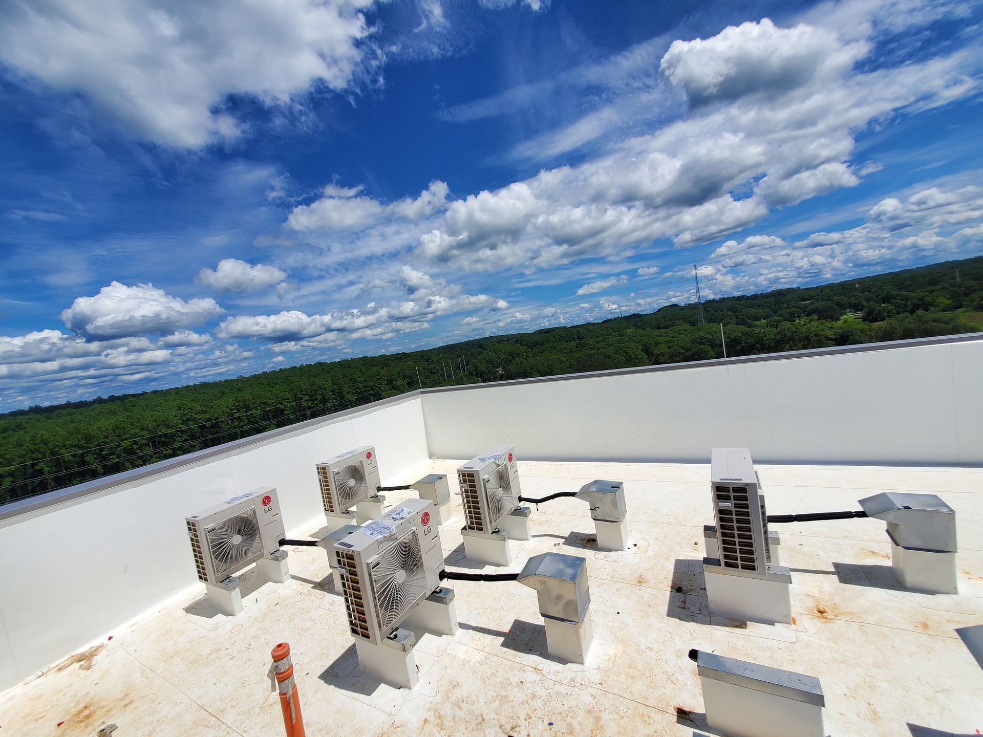 White rooftop with HVAC units against a blue sky with fluffy clouds; distant green trees.
