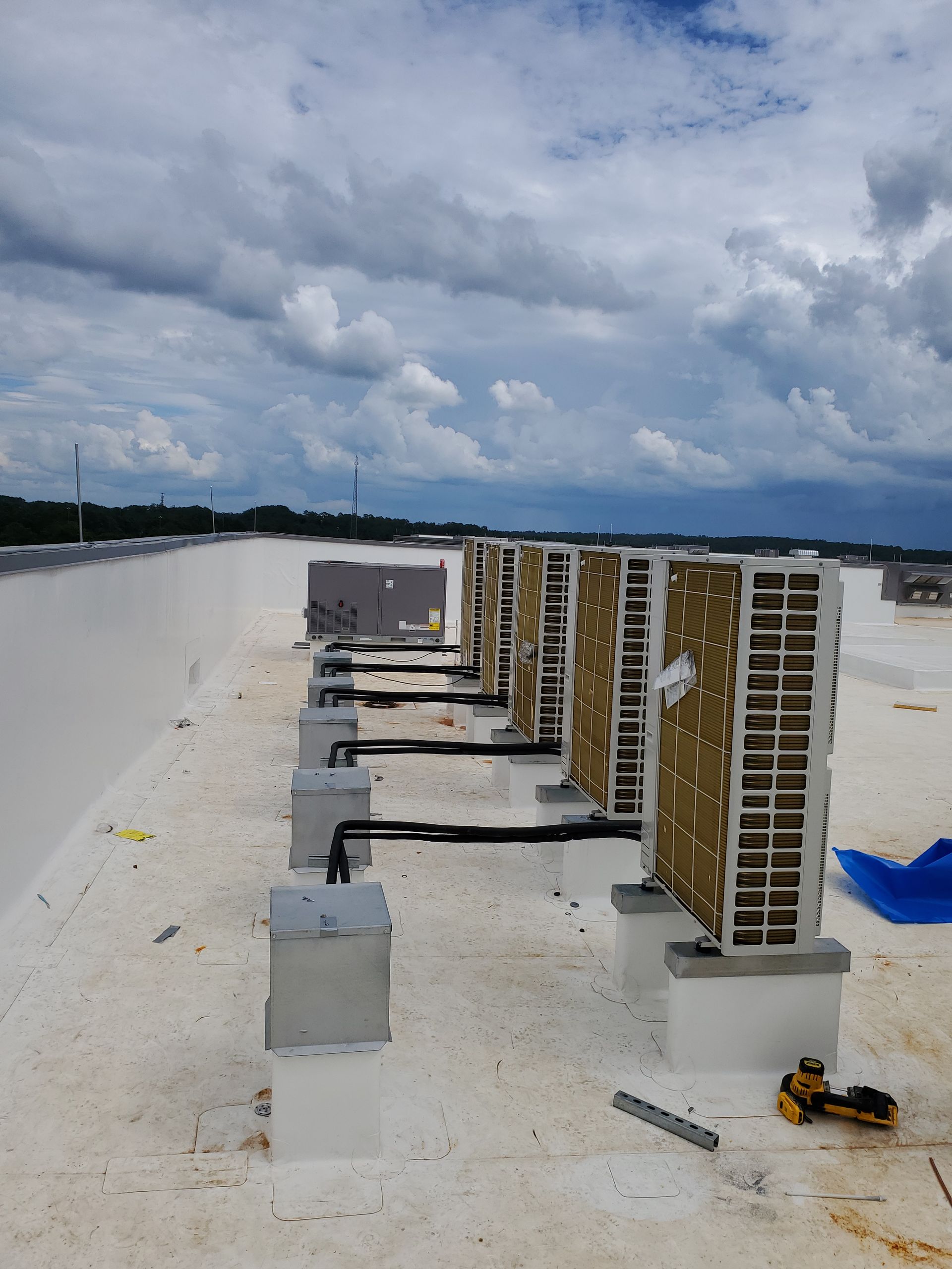 Rooftop with several industrial air conditioning units and a cloudy sky.