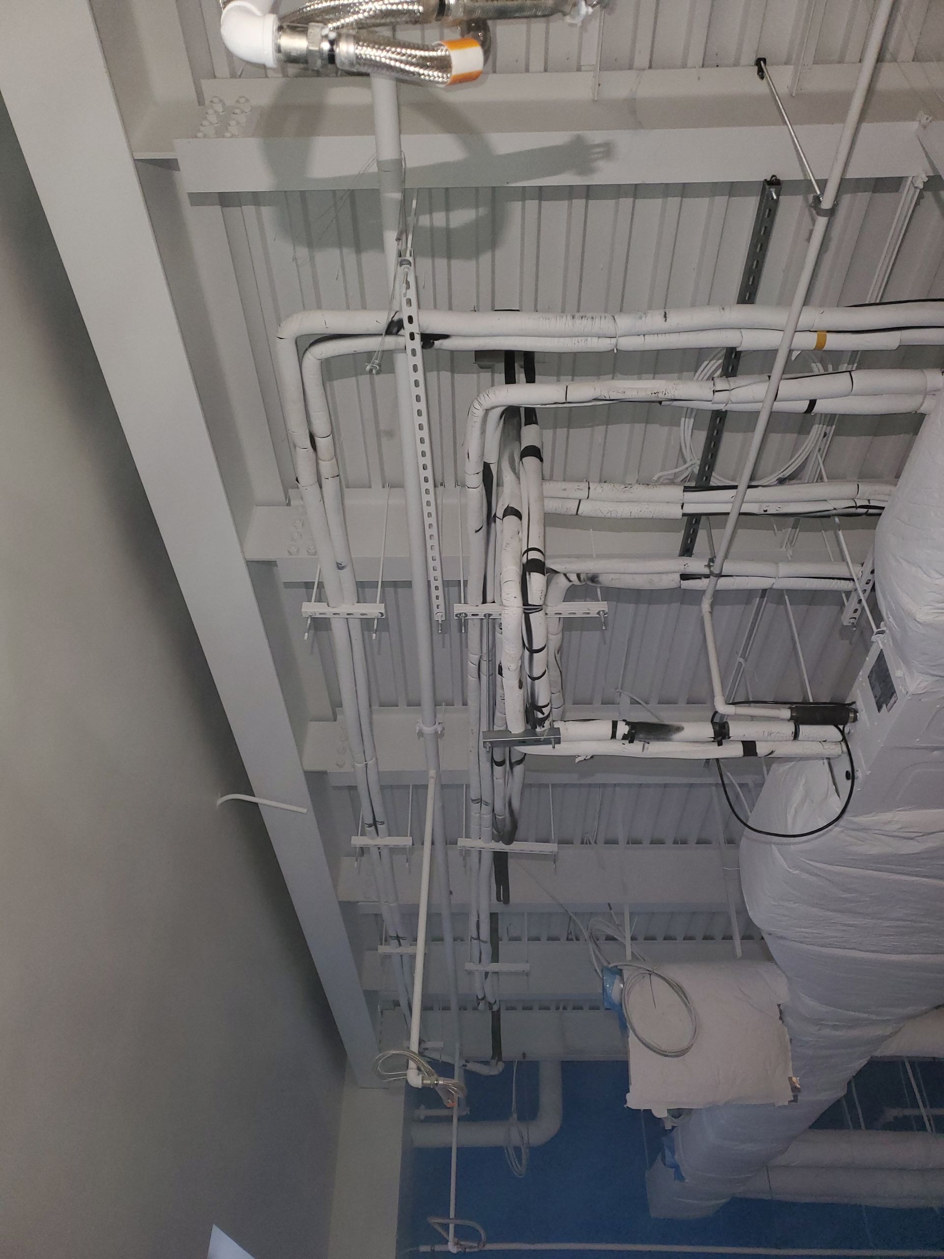 Overhead view of a ceiling with exposed pipes, ducts, and wiring painted white.