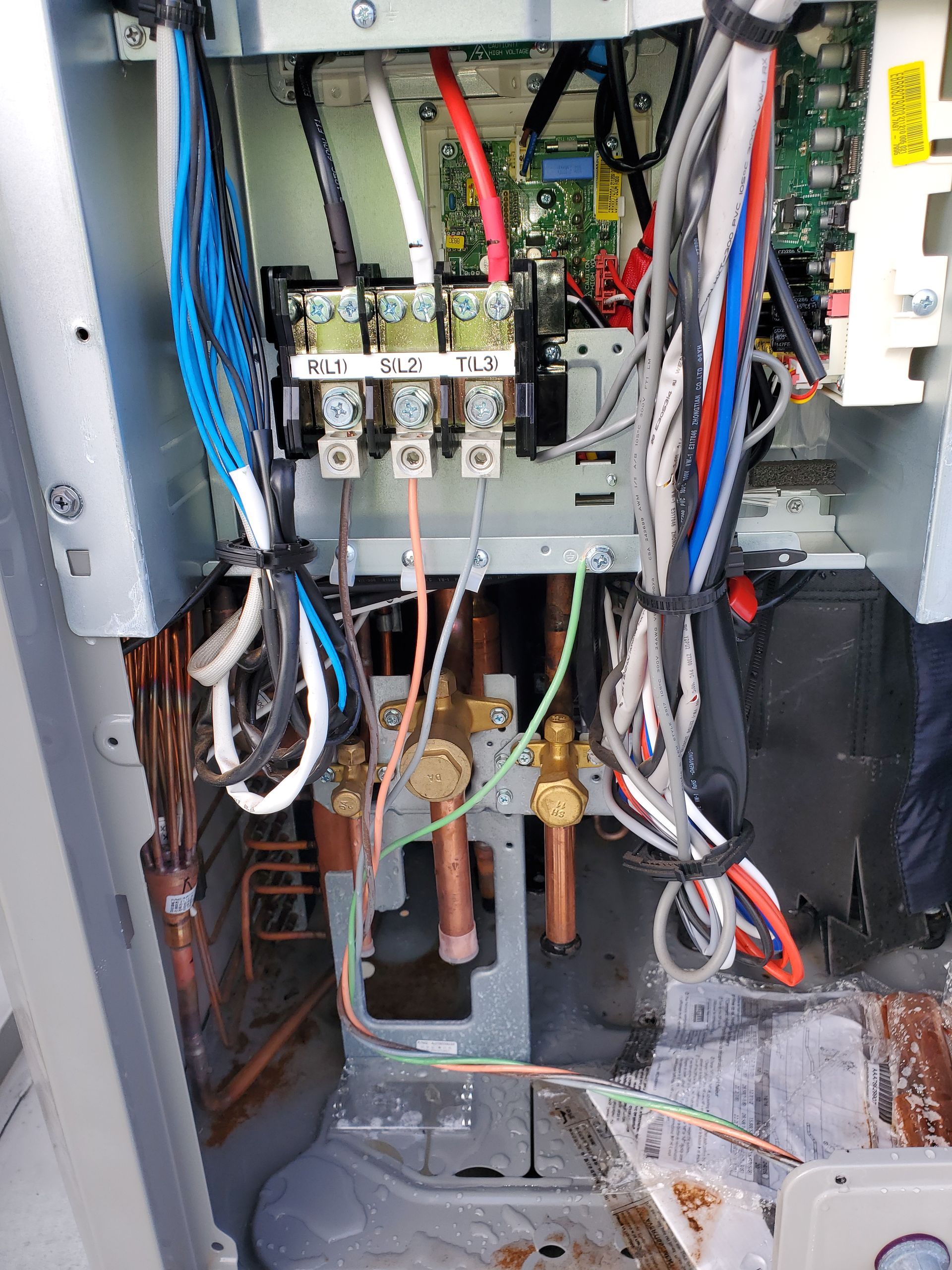 Close-up of electrical components and copper pipes inside an air conditioning unit's service panel.