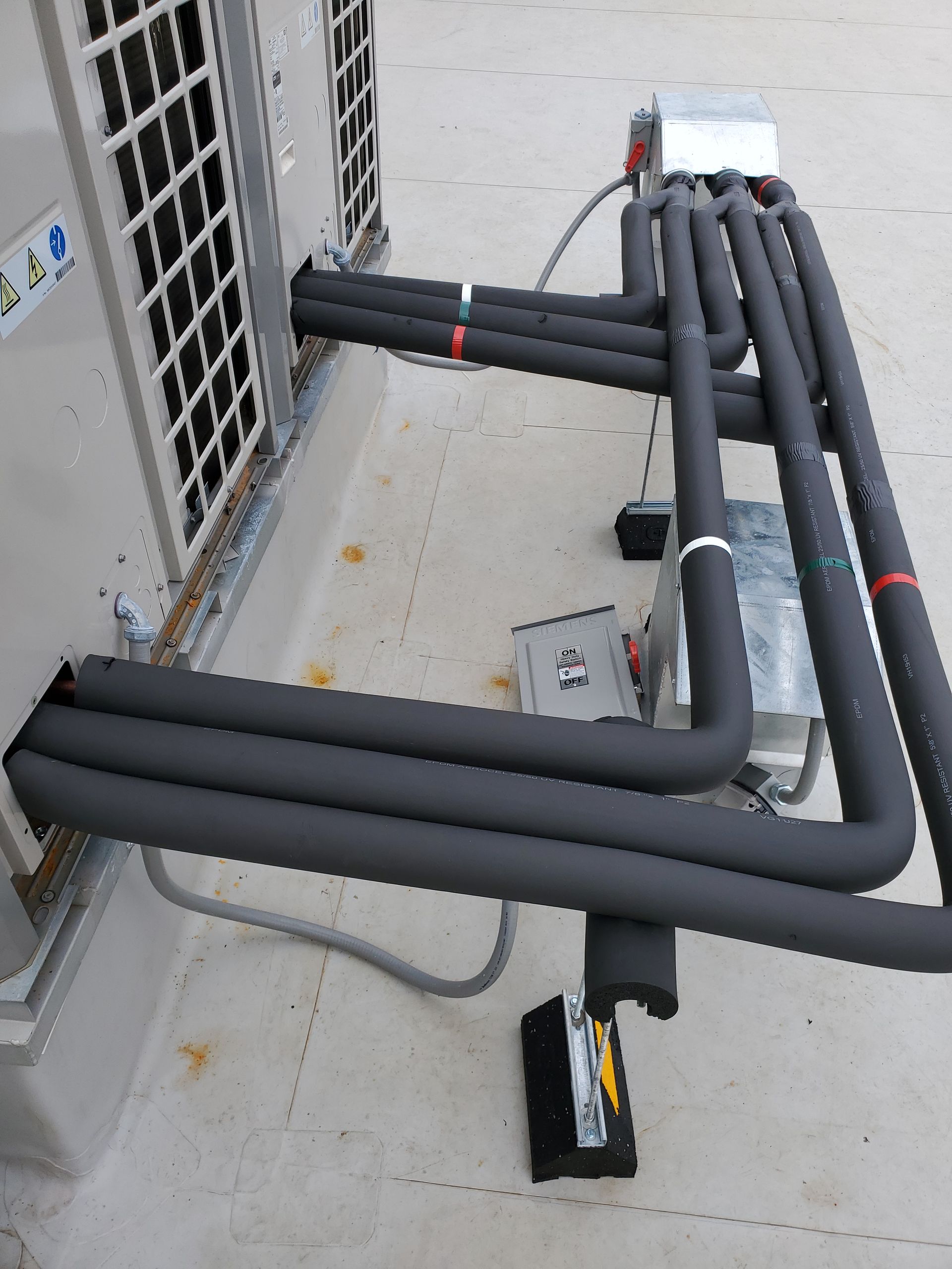 Air conditioning unit with insulated black pipes connected on a rooftop.