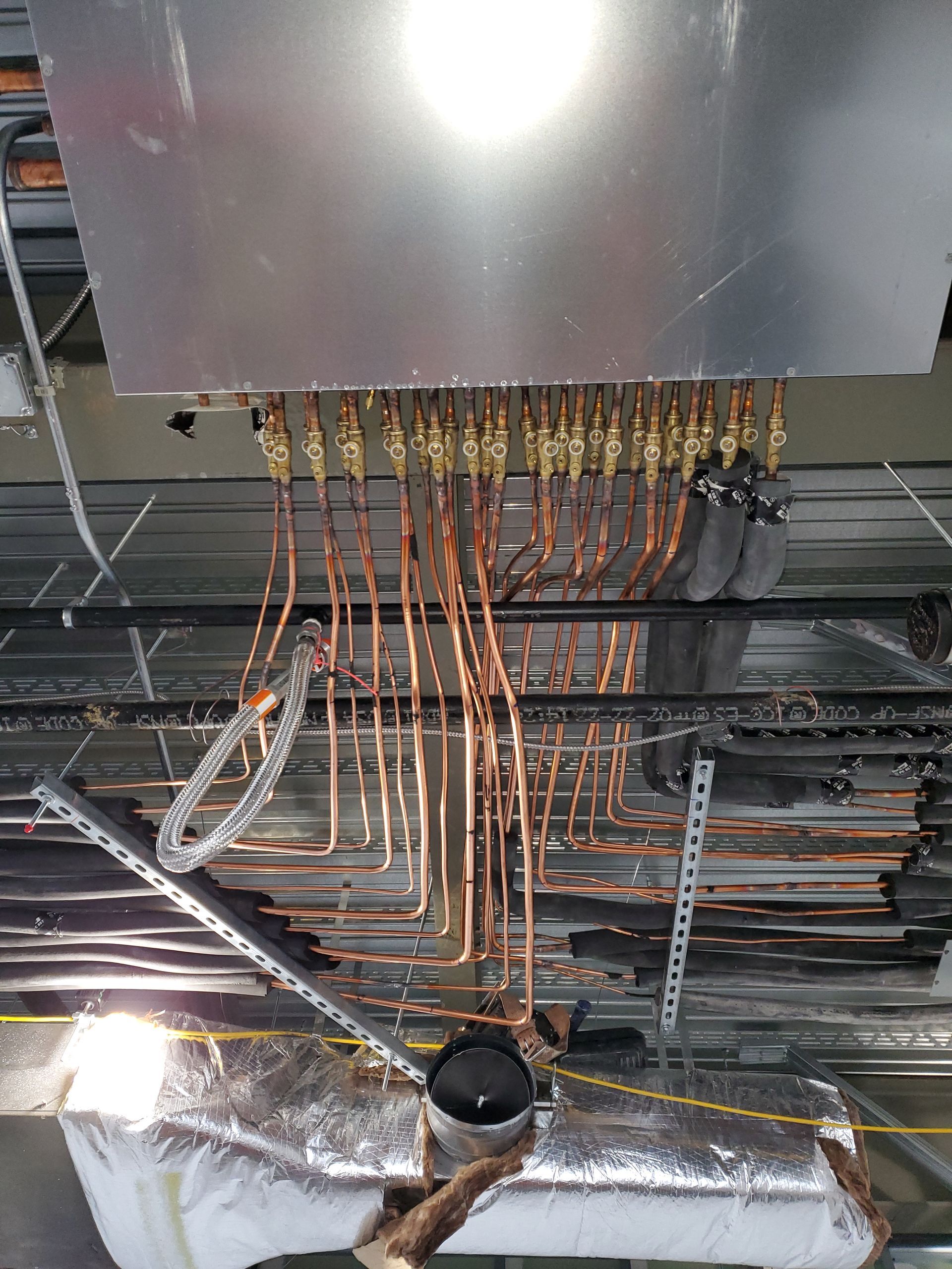 Copper pipes connected to a silver box, likely part of an HVAC system, installed in a ceiling.