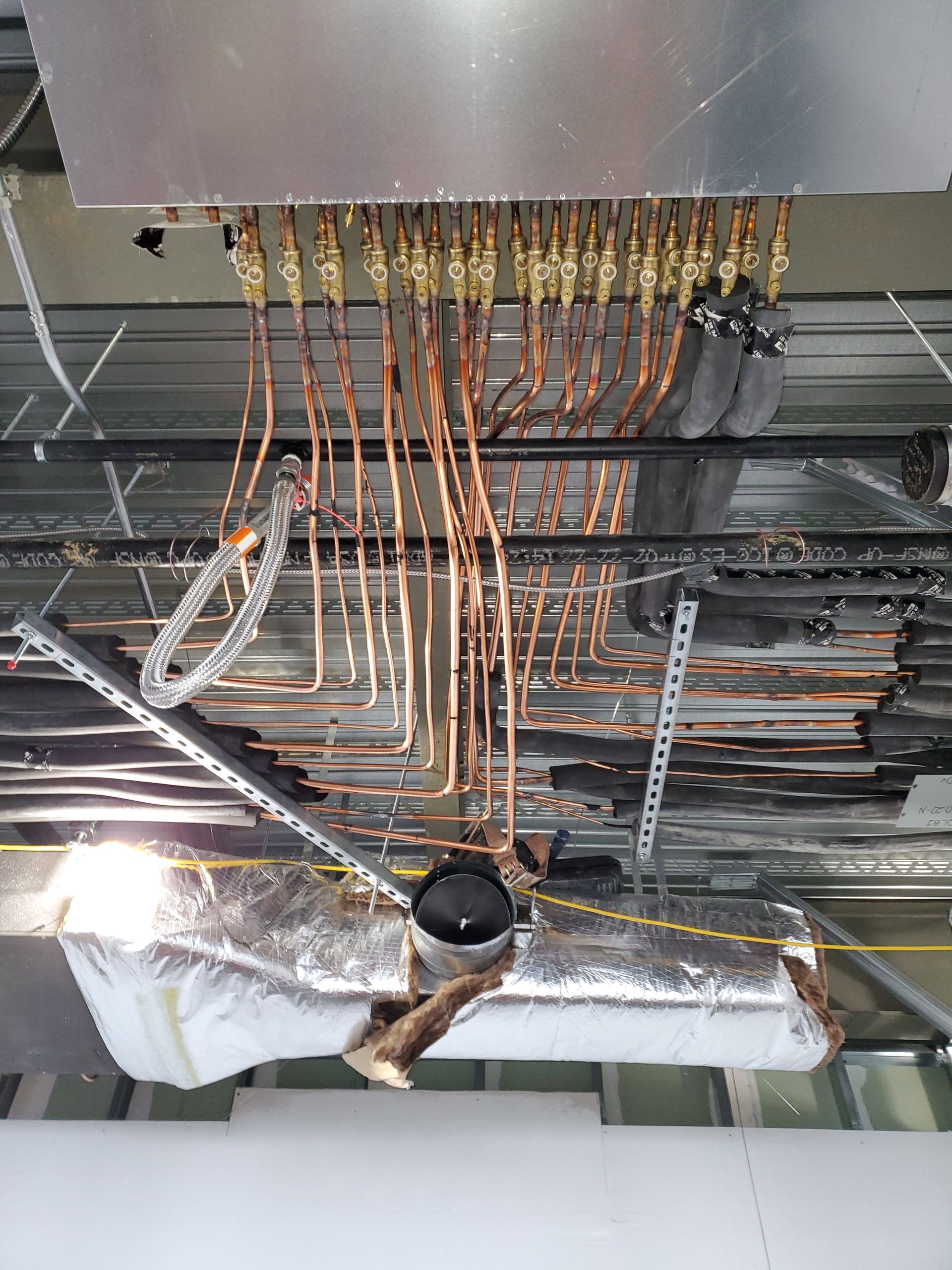 Copper pipes and valves attached to a metal box, ceiling installation in a building.