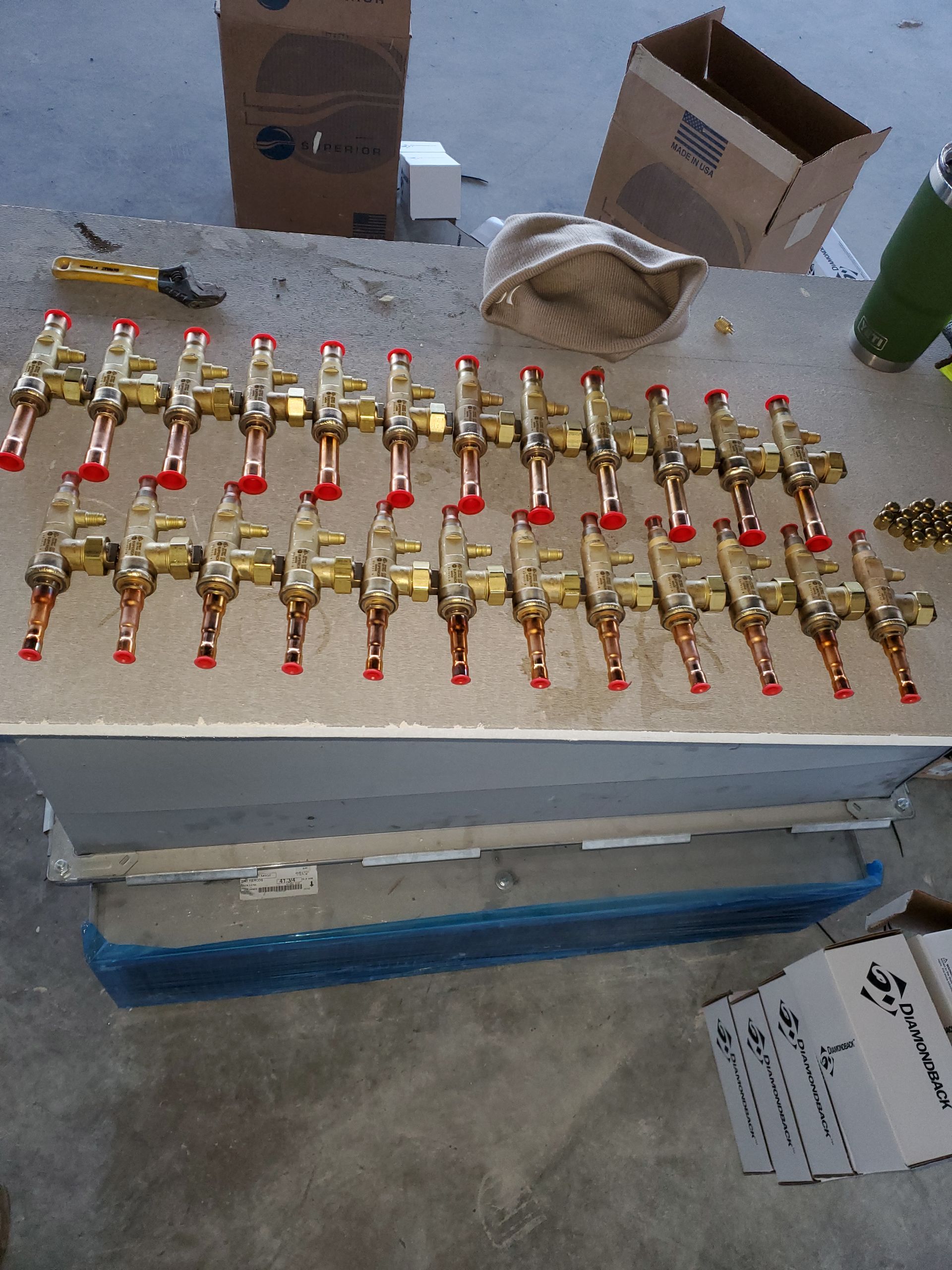 Rows of gold-colored valves with red handles arranged on a surface, with boxes and tools in the background.