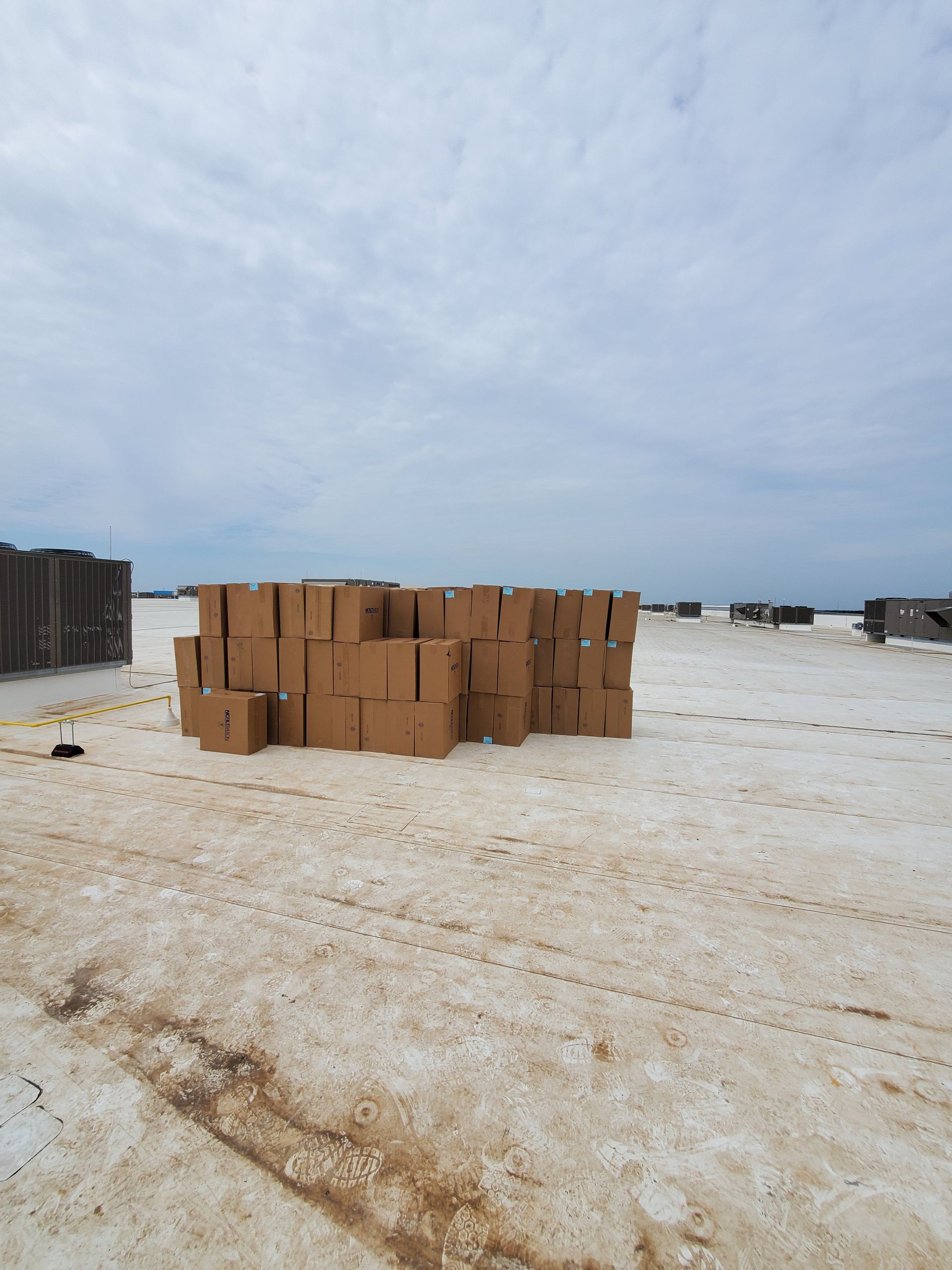 Cardboard boxes stacked outdoors on a white, possibly frozen, surface under a cloudy sky.