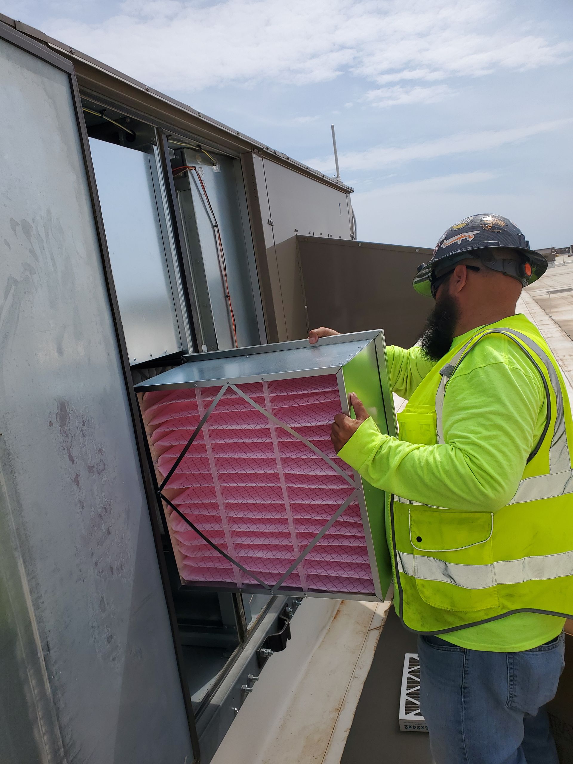 Person in safety vest replaces an air filter on a rooftop unit.