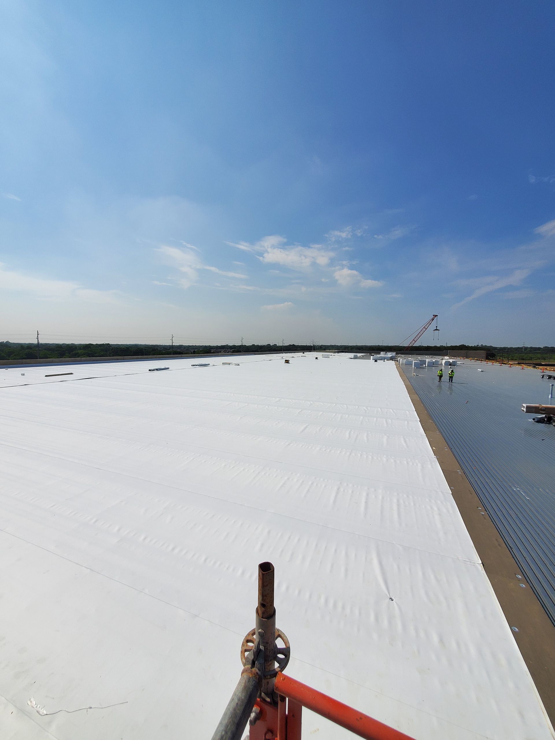 White fabric covers a large construction area under a blue sky, workers visible in the distance.