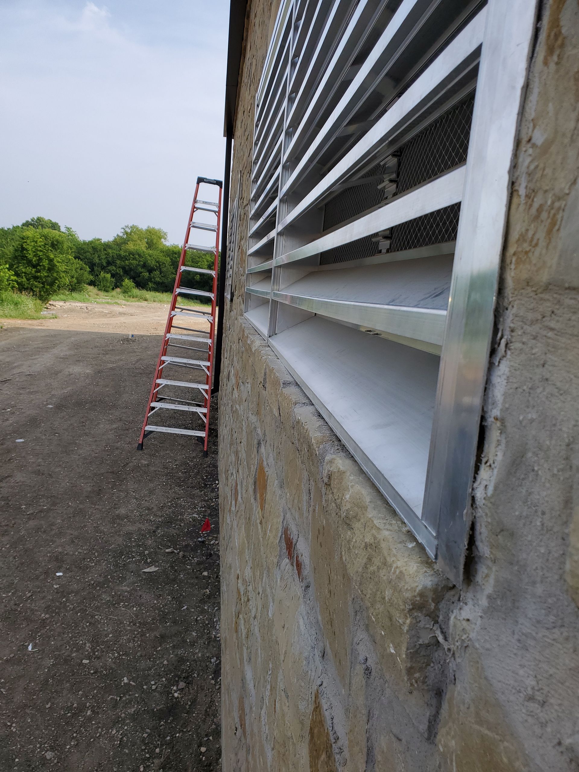 Exterior wall with a louvered window, aluminum frame, and a ladder leaning against the side.