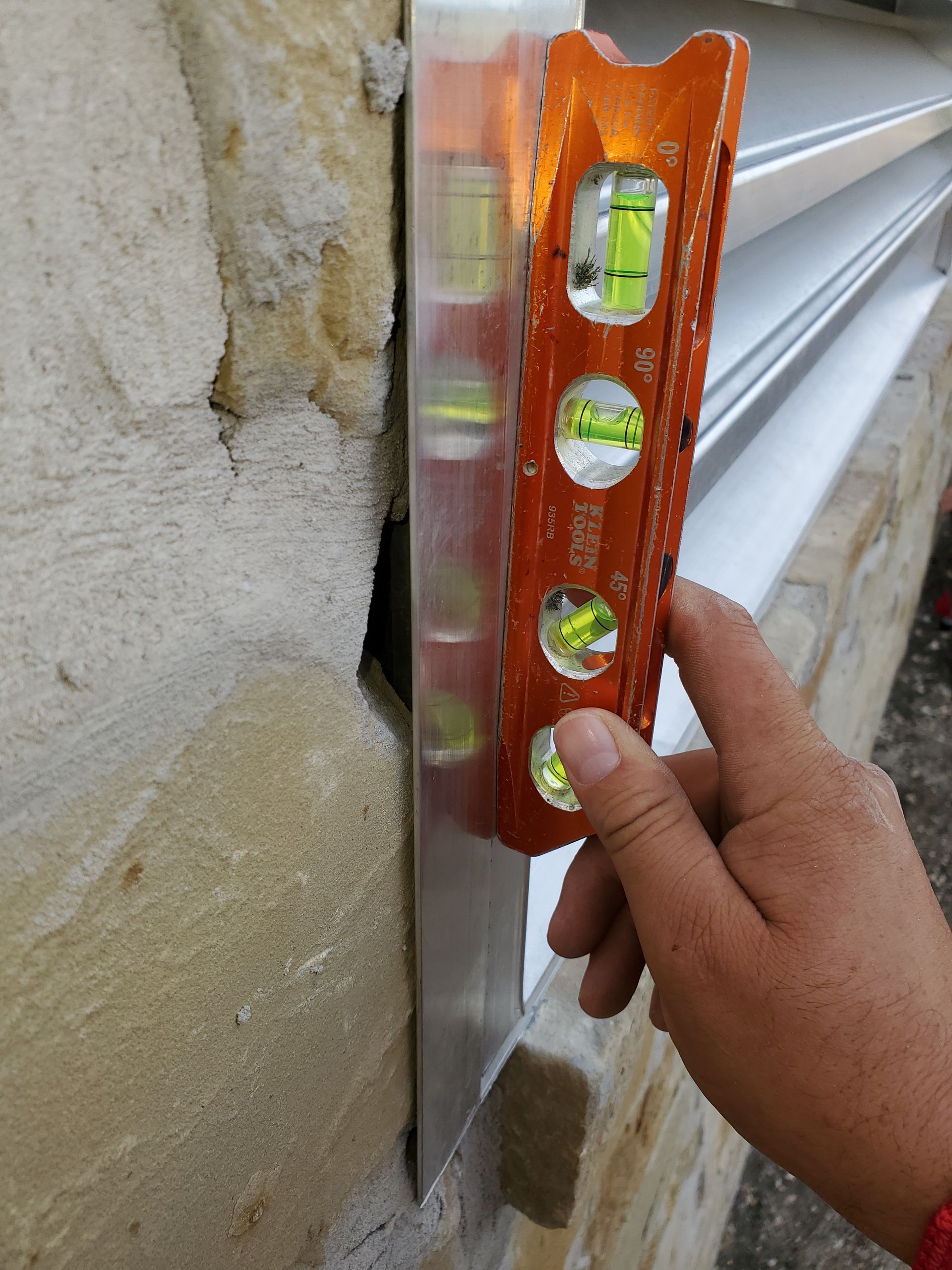 Hand holding a level against stone wall and metal edging; bubbles show vertical alignment.