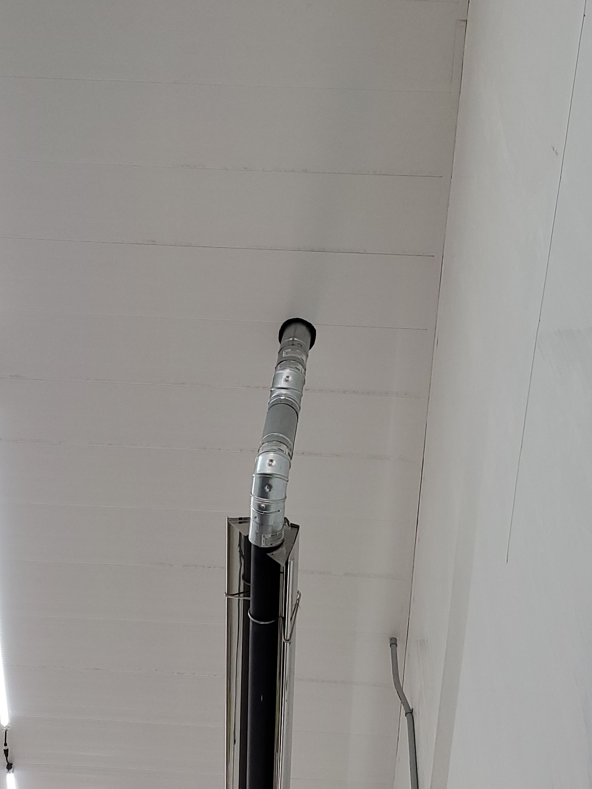 Metal stove pipe exiting through white ceiling.