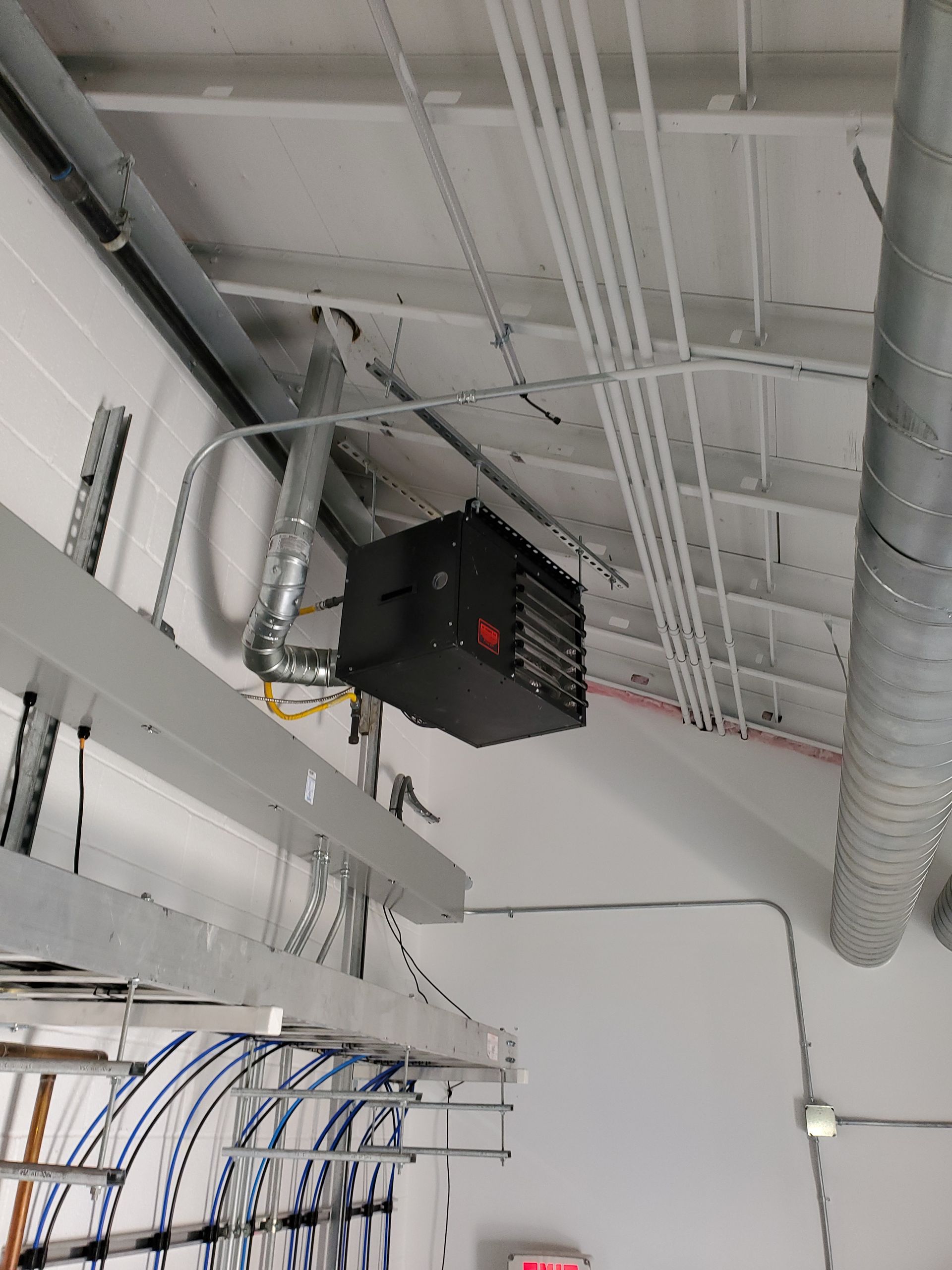 Black industrial heater mounted on a white ceiling with ductwork and conduit visible.