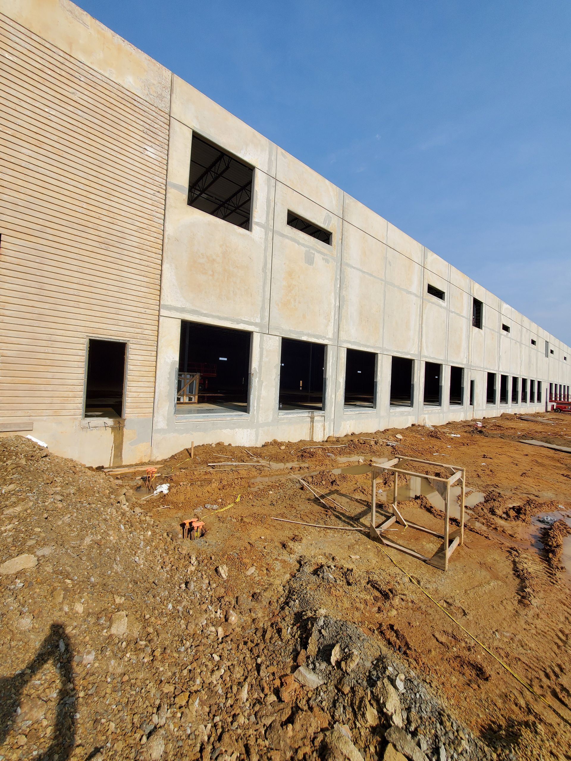 Exterior of a building under construction, with concrete walls, window frames, and dirt ground.