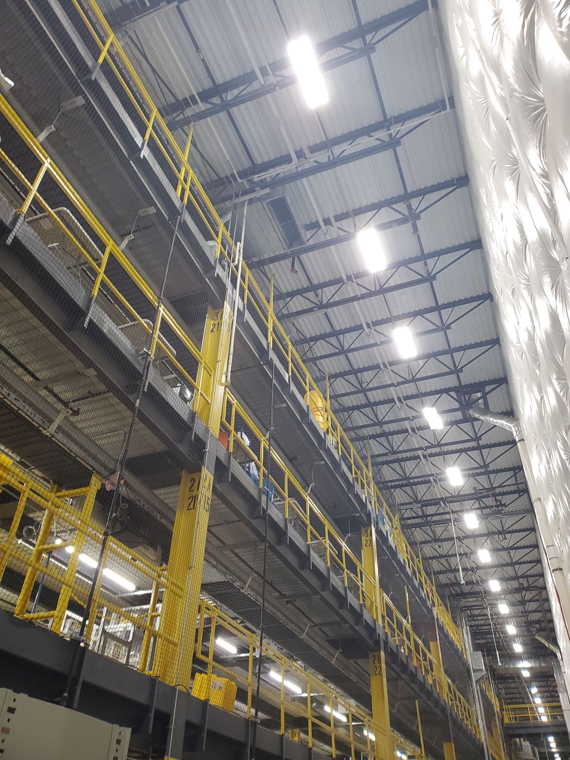 Yellow elevated walkways inside a warehouse, with metal beams, lighting, and a high ceiling.