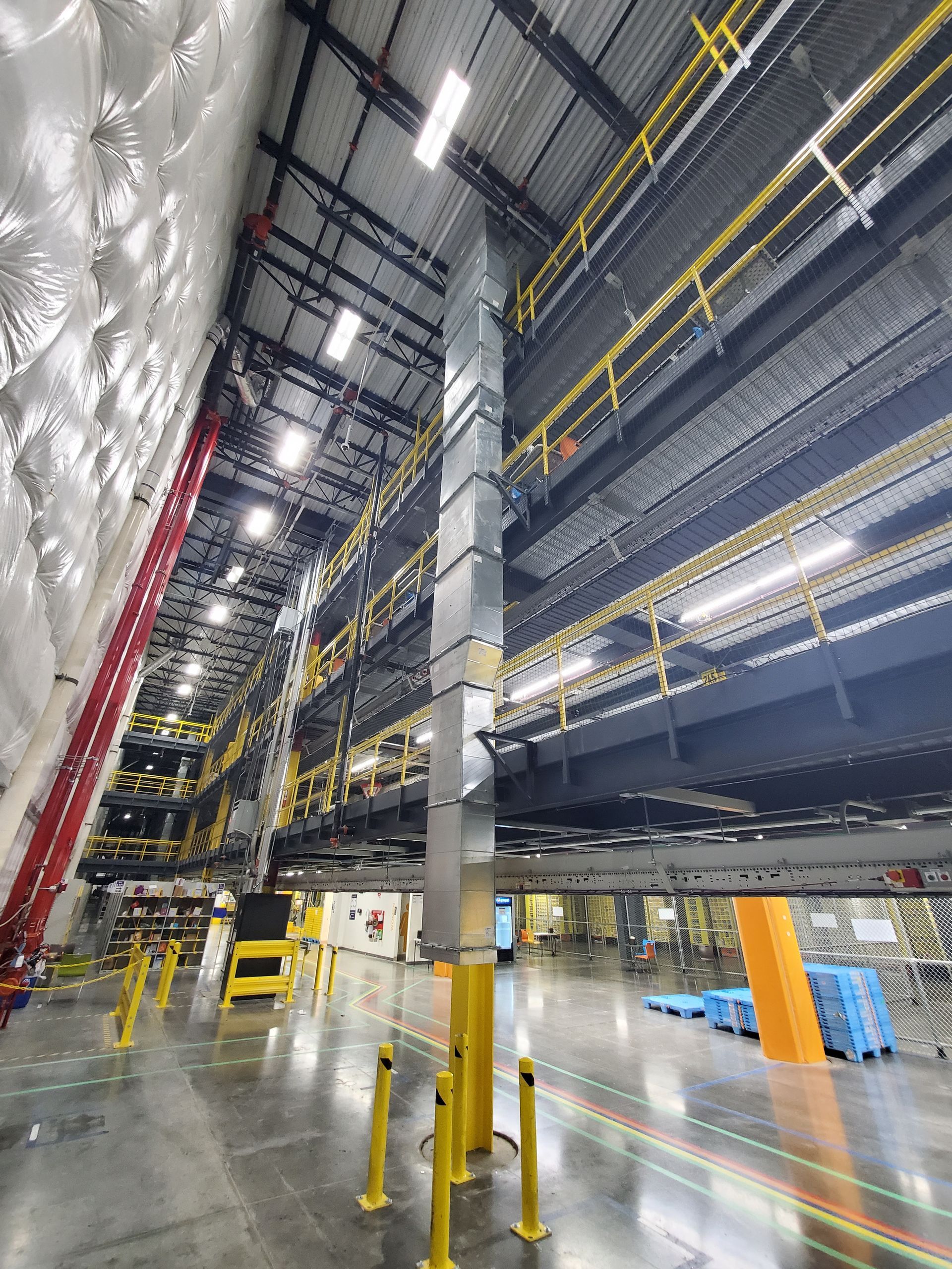 Inside of a multi-level industrial warehouse with shelving, metal support beams, and exposed ductwork.