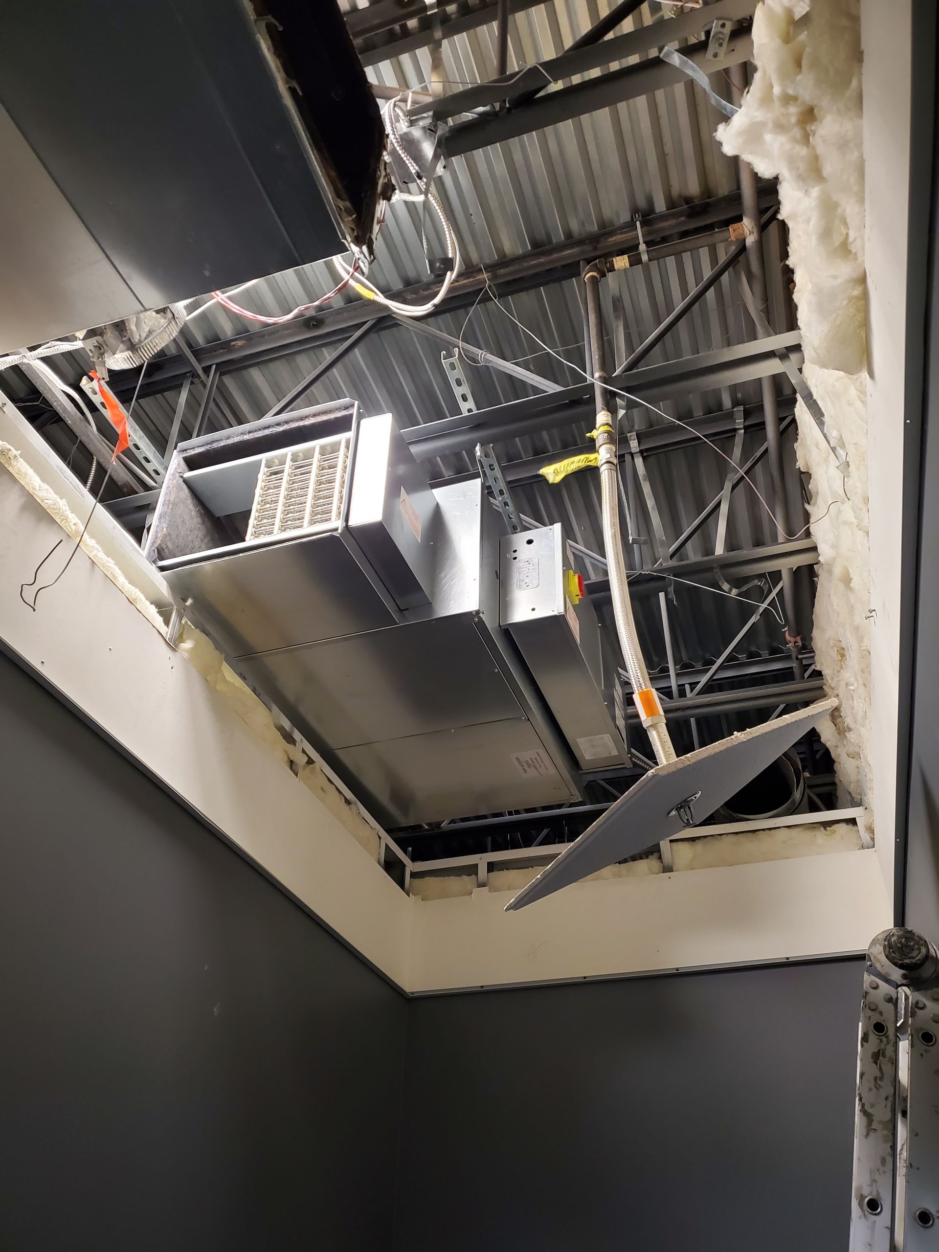 Ceiling damage reveals HVAC ductwork and wires. Gray room with damaged white wall and insulation visible.