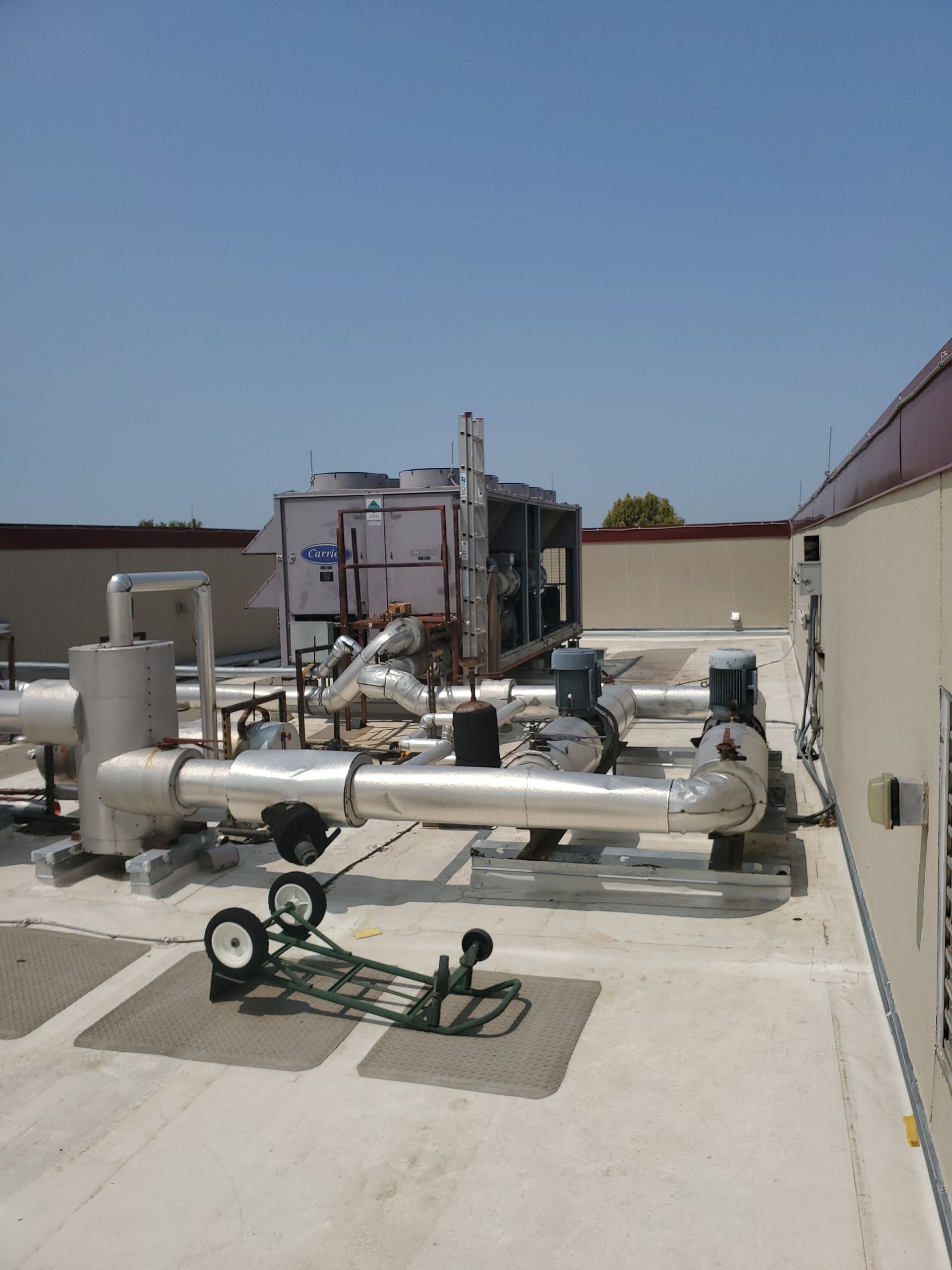 Rooftop HVAC equipment with pipes and pumps under a clear blue sky.