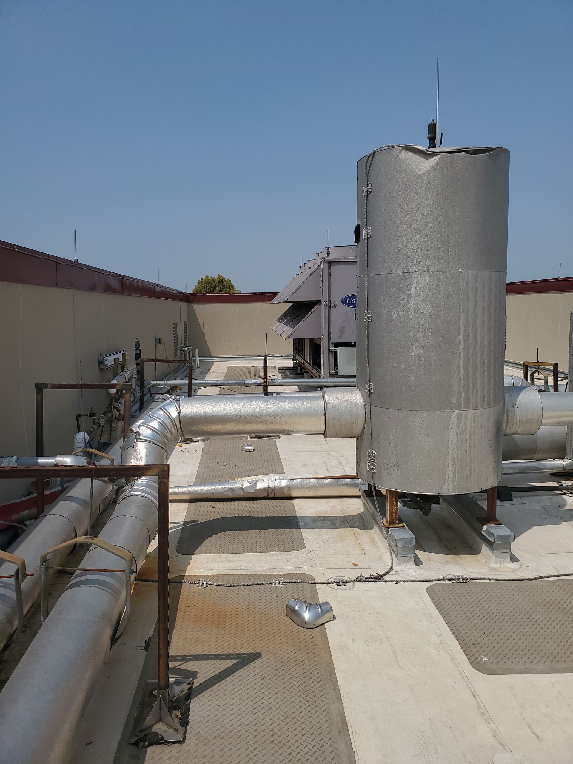 HVAC equipment on a flat roof. Insulated pipes and a cylindrical unit. Sunny day, clear sky.