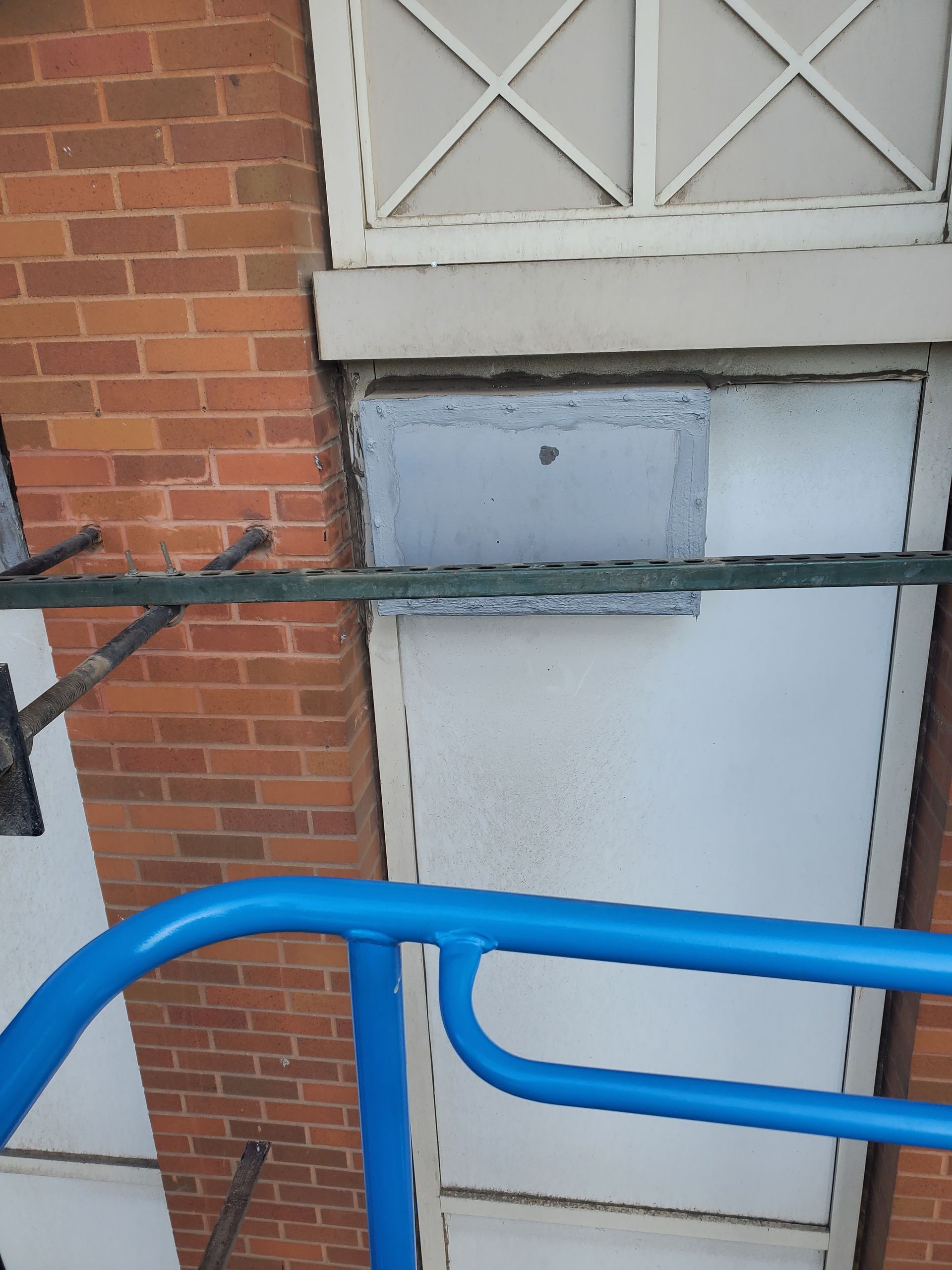 Brick wall with a white door and window; a blue railing in the foreground.