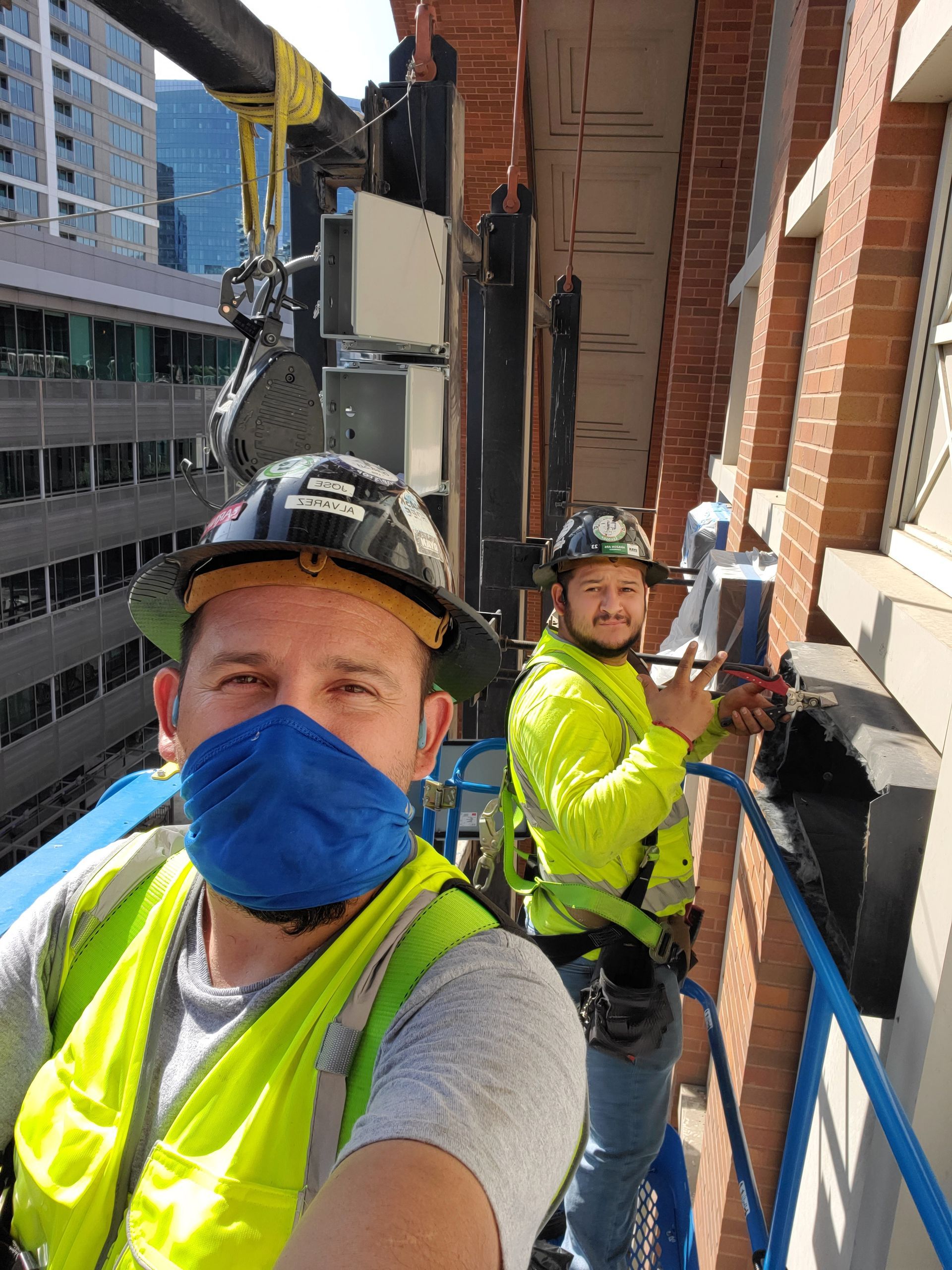 Two construction workers in safety gear on a lift working on a brick building facade.