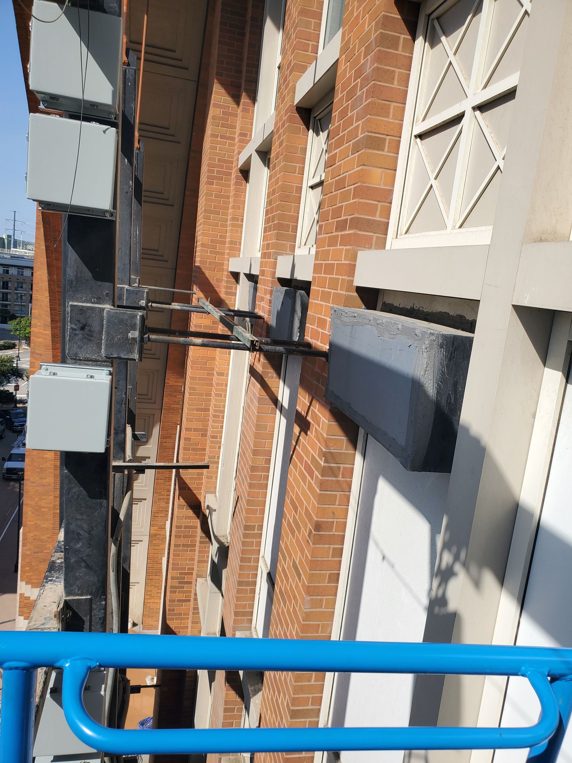 Exterior of a brick building with gray concrete supports and a blue railing in the foreground.