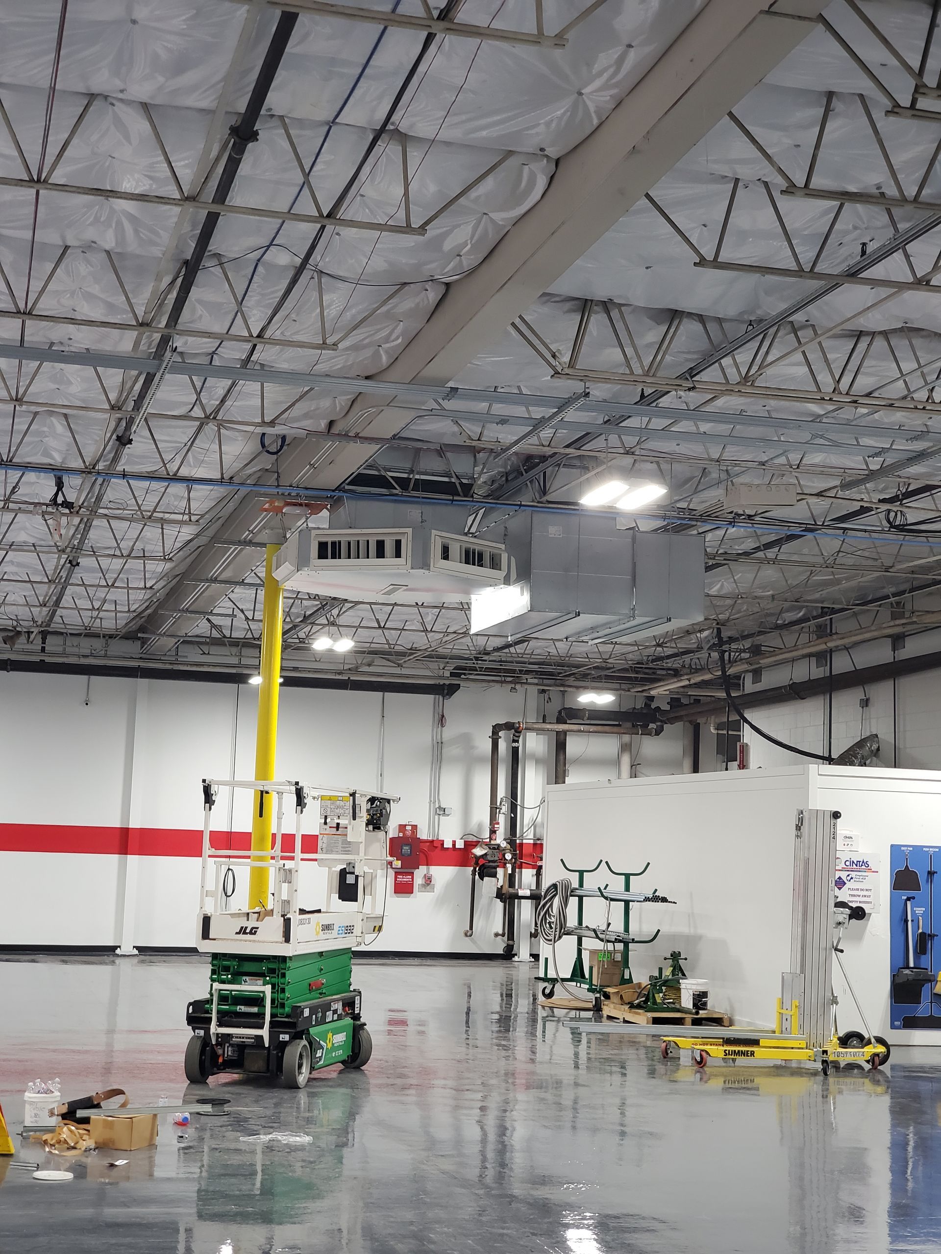 A scissor lift in an industrial space, near a red stripe on a wall. Shiny floor reflects the ceiling.