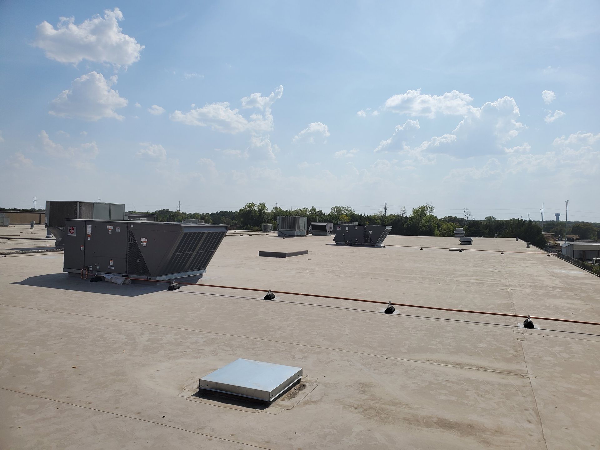 Flat commercial roof with HVAC units under a blue sky with clouds.