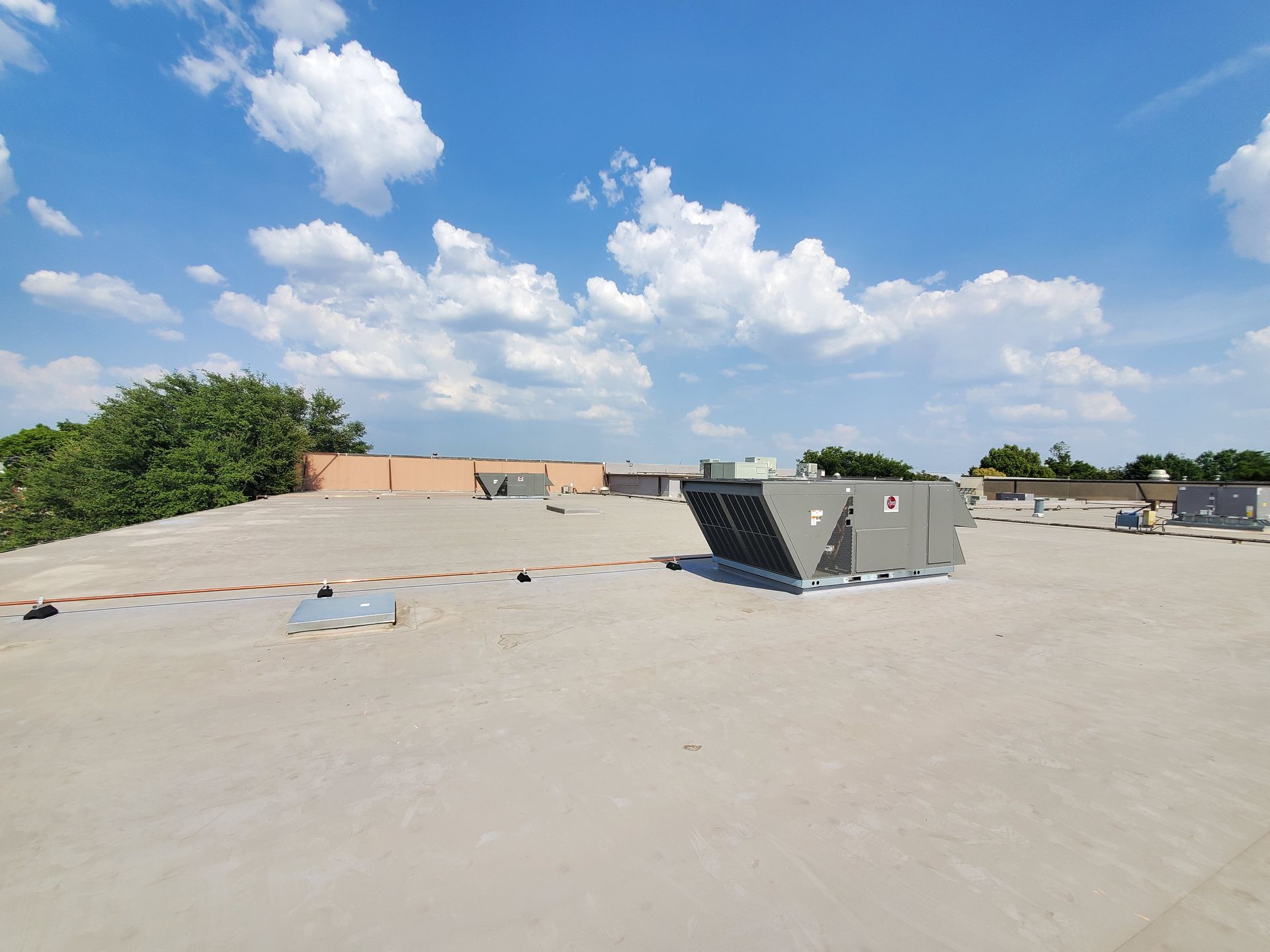 Flat rooftop with HVAC units against a blue sky with scattered clouds.