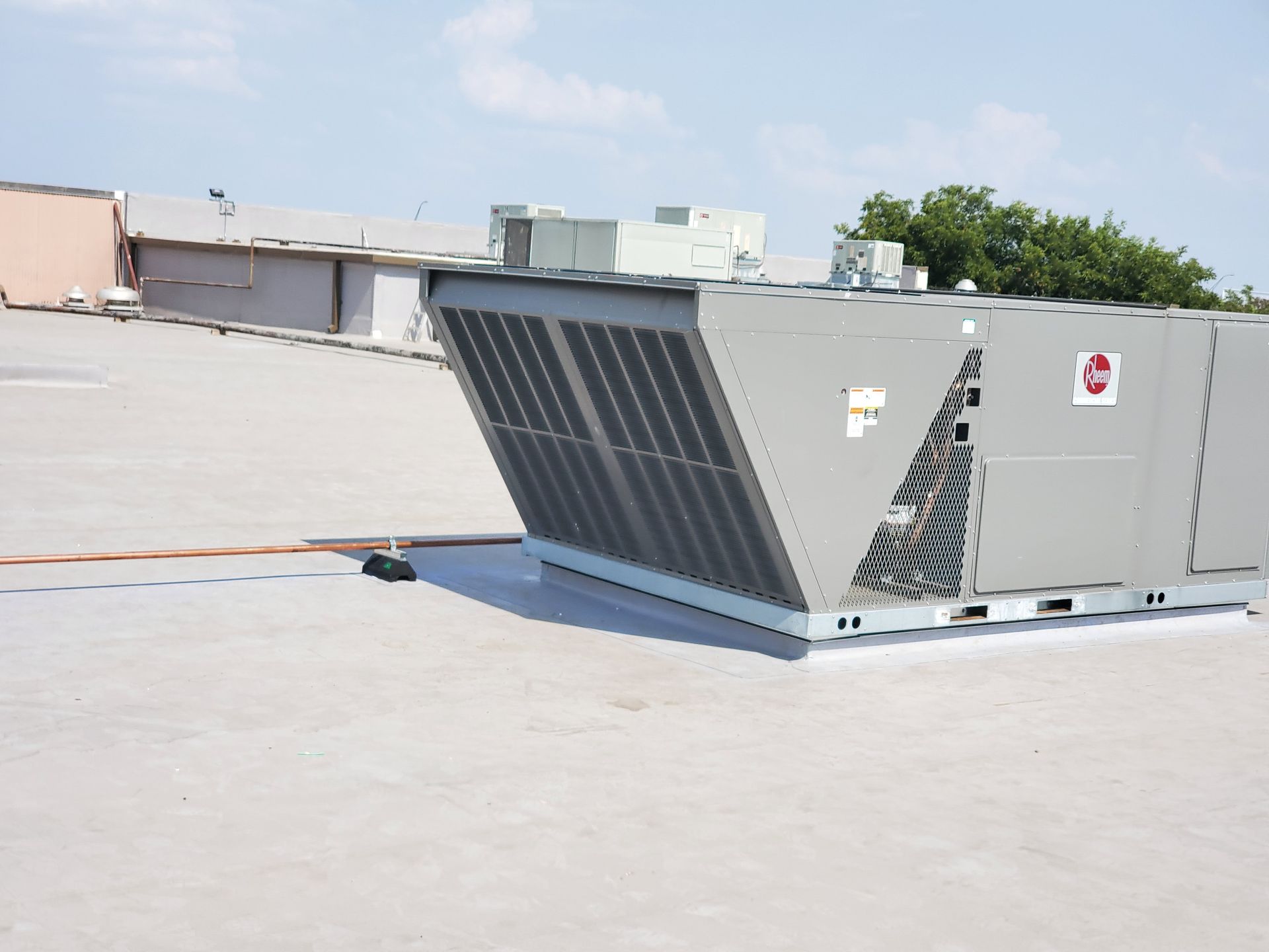 HVAC unit on a flat white roof with other rooftop structures under a blue sky.