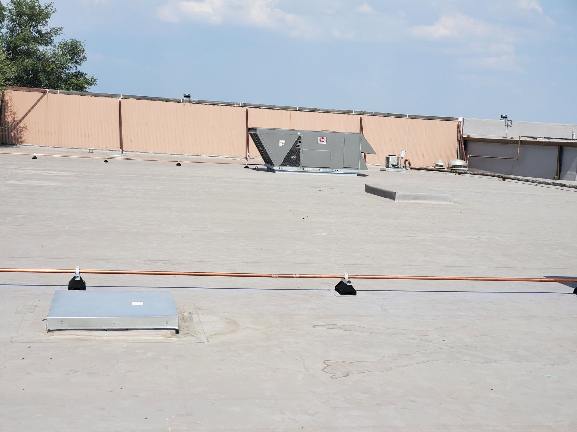 Rooftop with HVAC units, vents, and a long copper wire running across. Beige walls and a cloudy sky in the background.