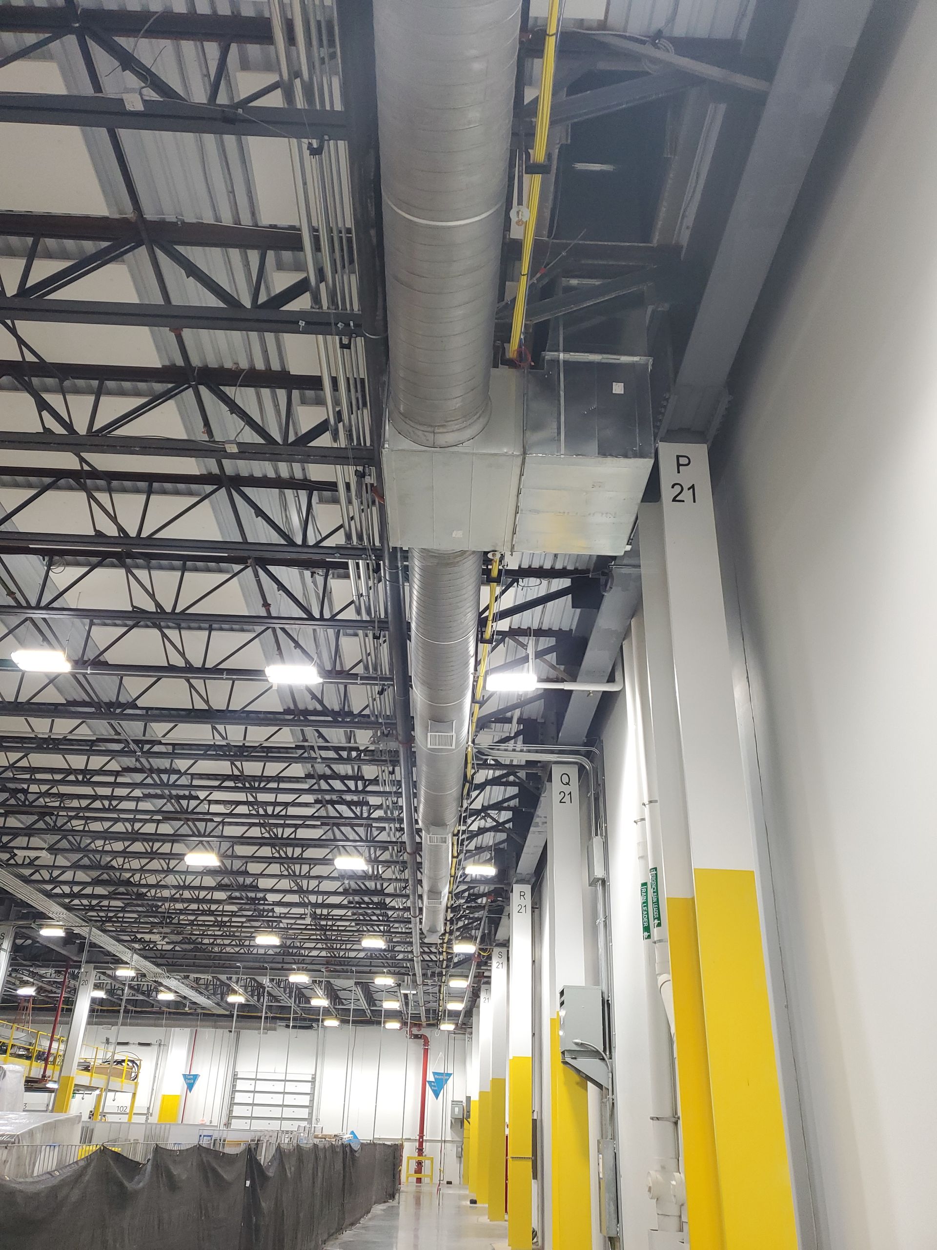HVAC ductwork and electrical wiring run along the ceiling of a warehouse with a loading dock.