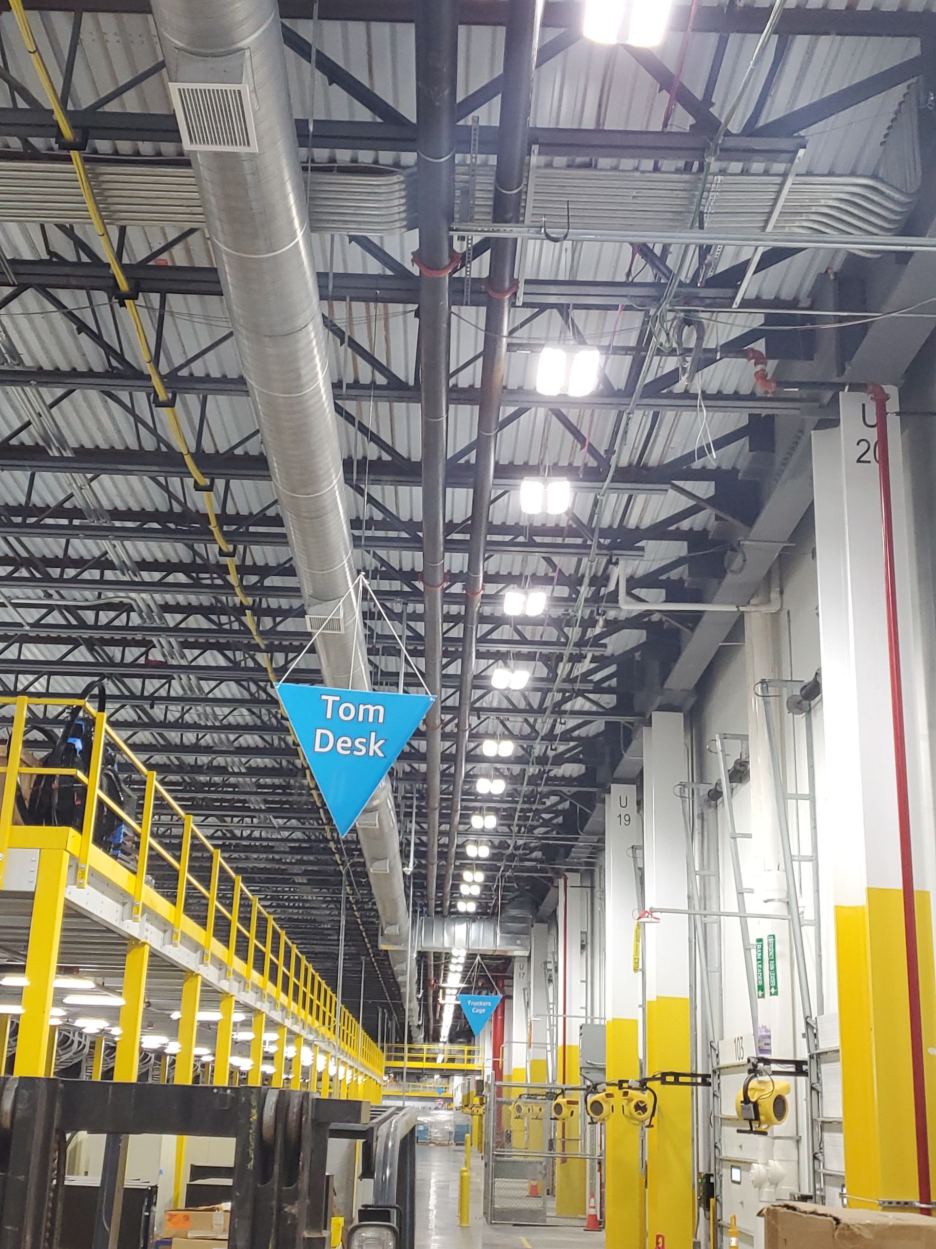 Warehouse interior with Tour Desk sign, metal ceiling beams, and yellow safety poles.