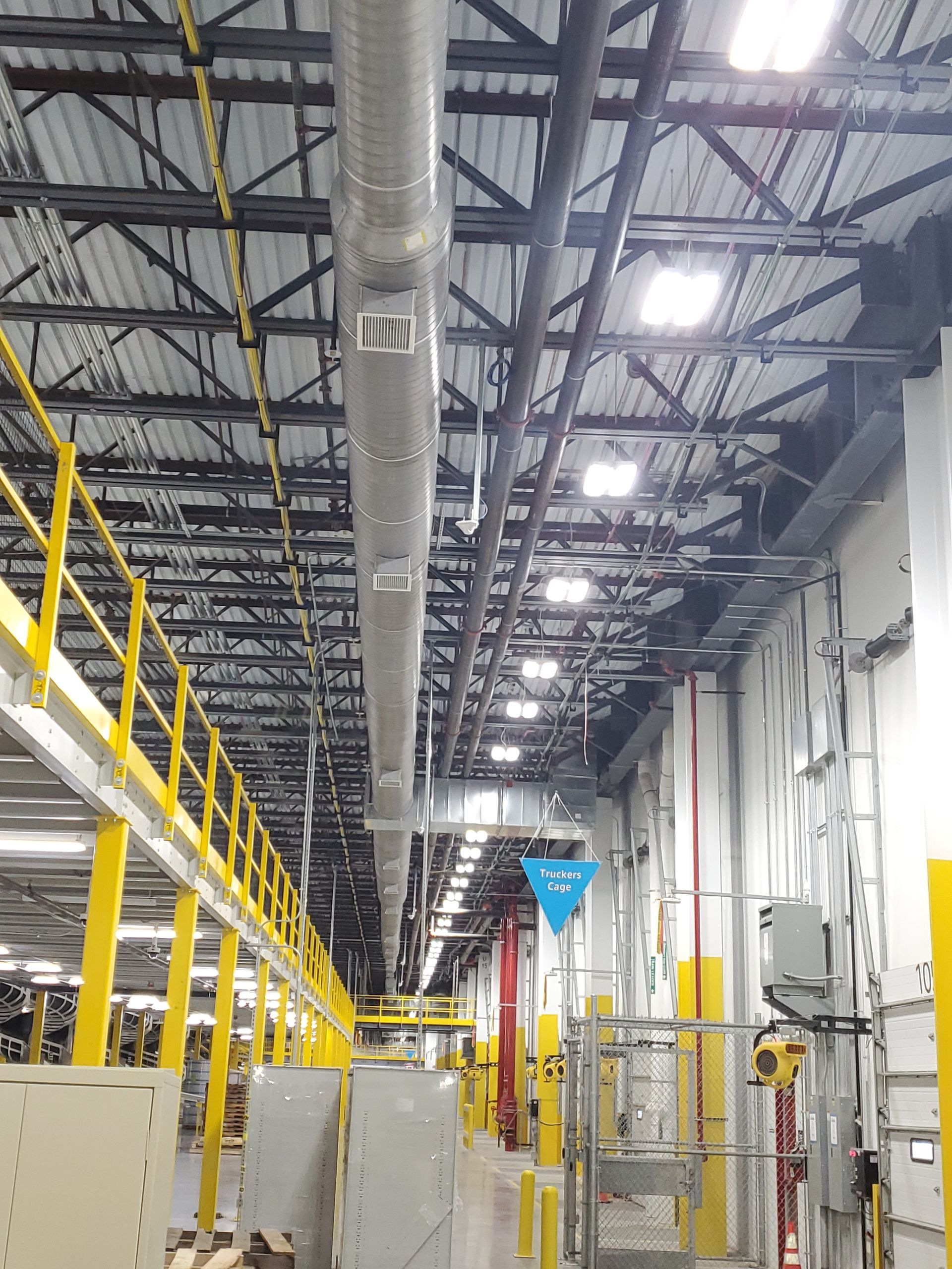 Warehouse interior with yellow railings, ventilation ducts, and overhead lighting.