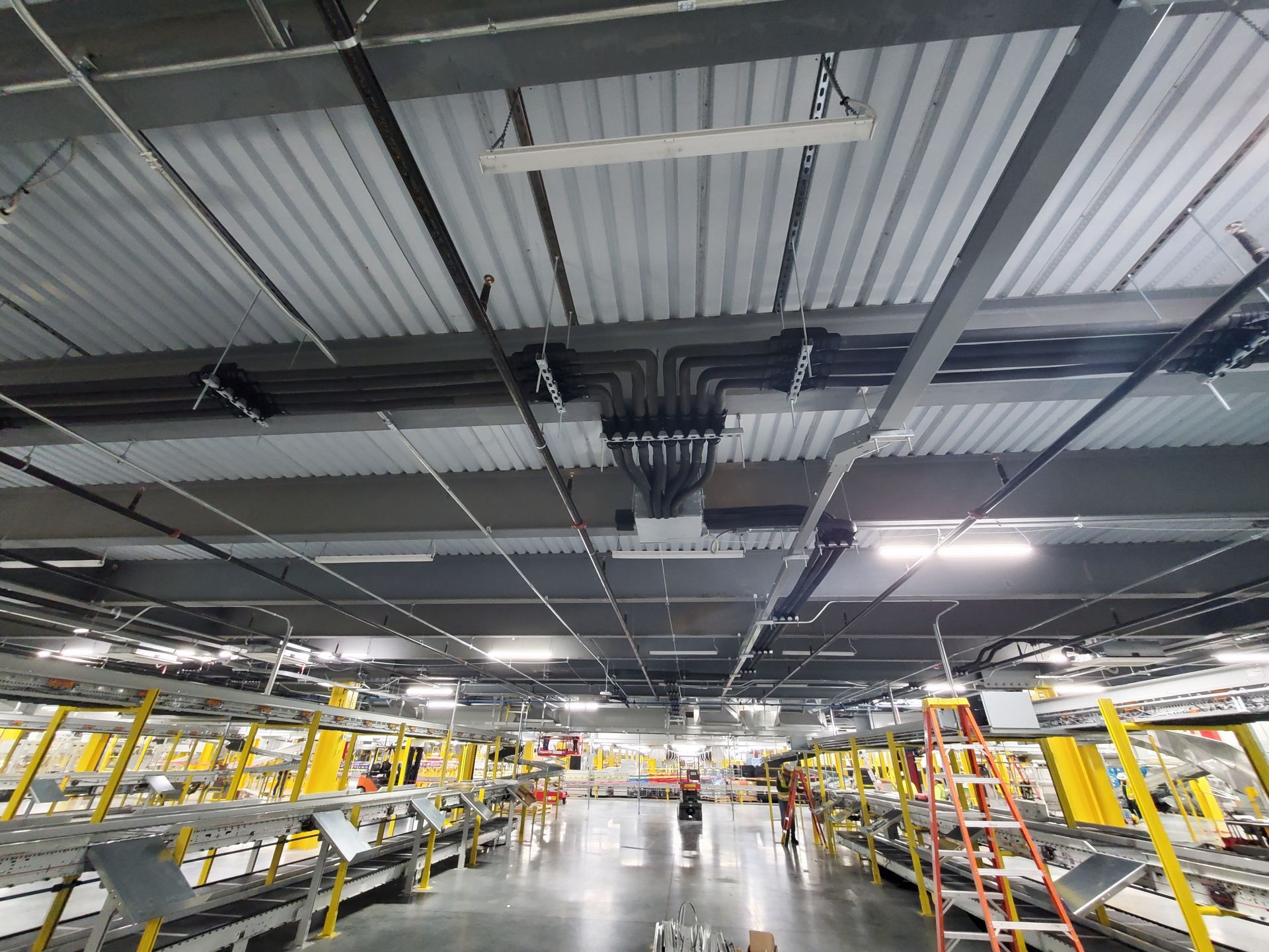 Industrial interior with corrugated ceiling, overhead wiring, and shelving units.