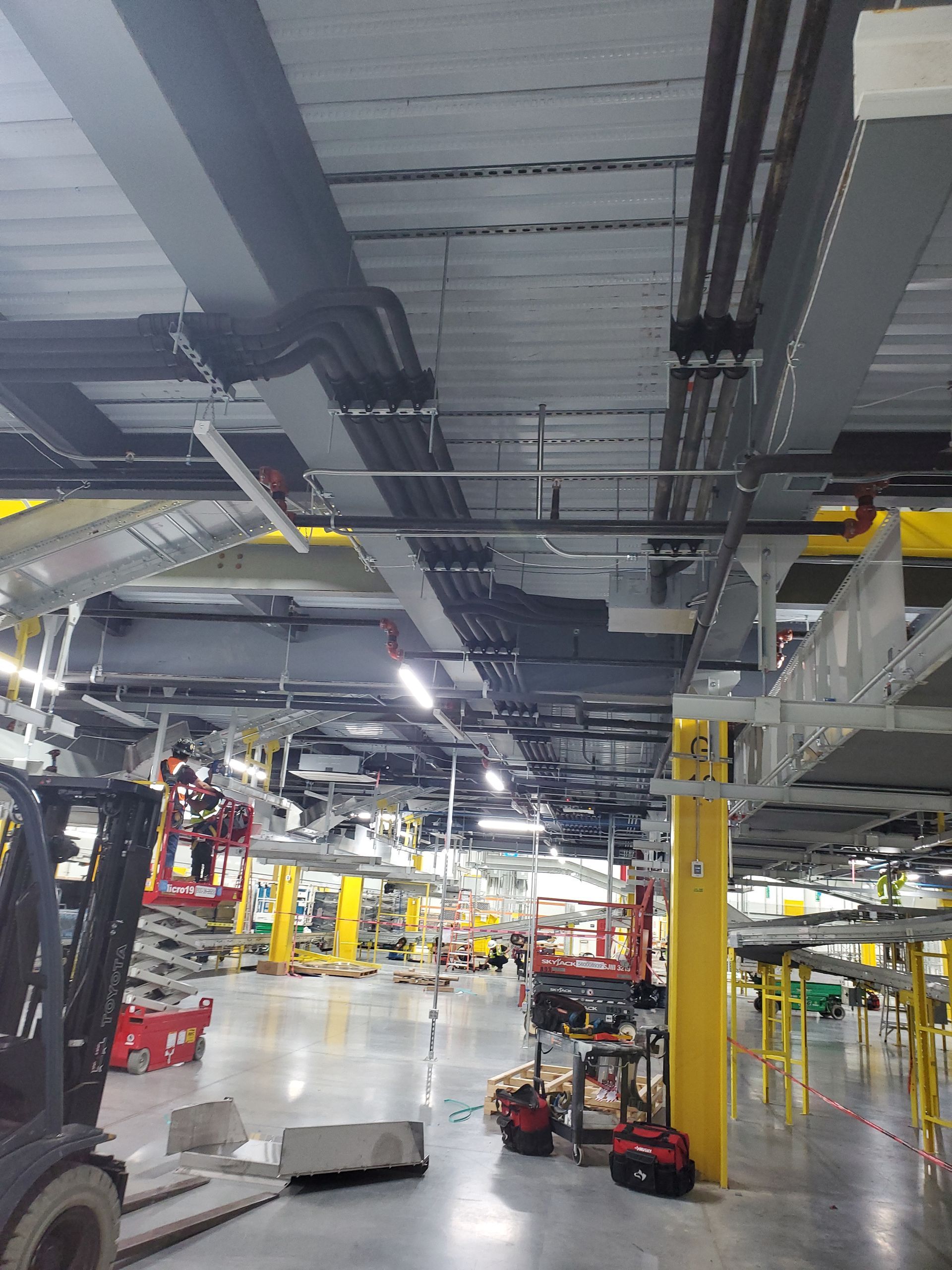 Factory interior with overhead wiring and equipment, multiple forklifts, and vehicles on a production line.
