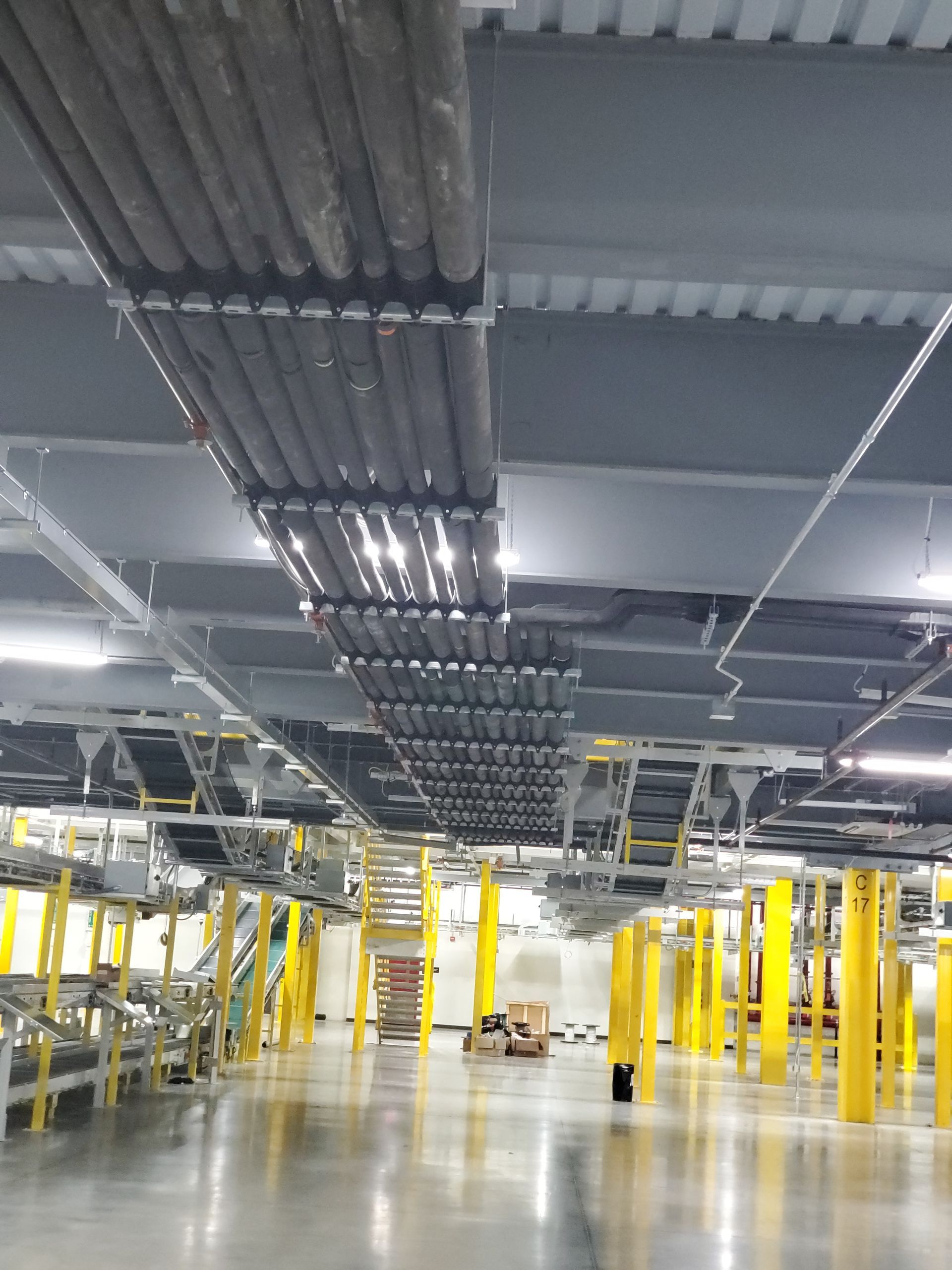 Overhead view of a warehouse interior with cables, support beams, yellow columns, and conveyor belts.
