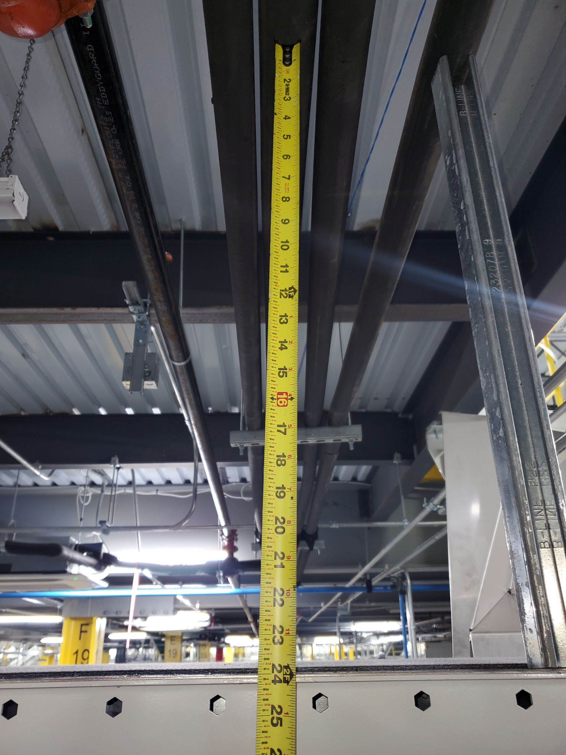 A yellow tape measure extends upwards in a warehouse, measuring the distance to the ceiling.