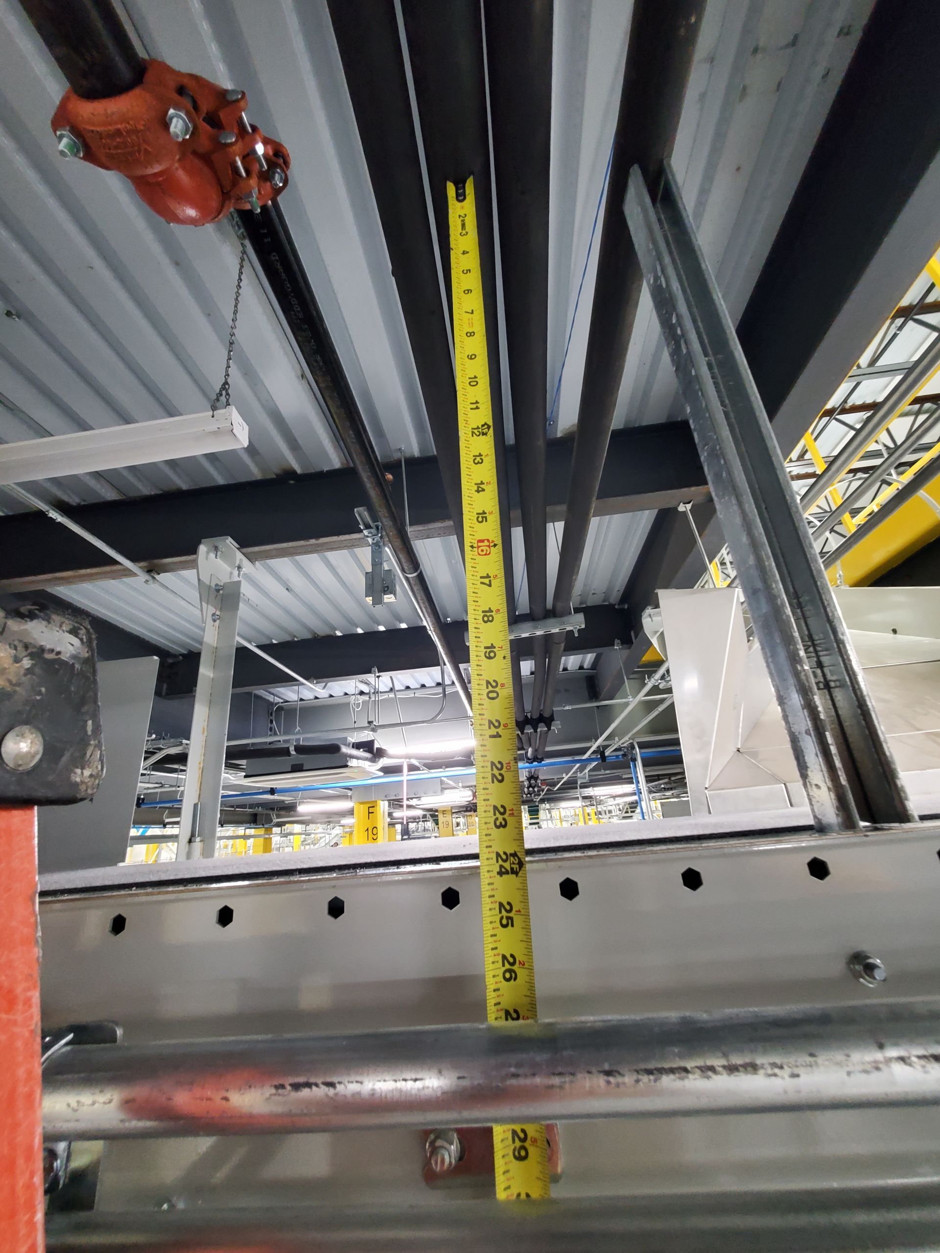 Tape measure extended, showing height between scaffolding and ceiling infrastructure.