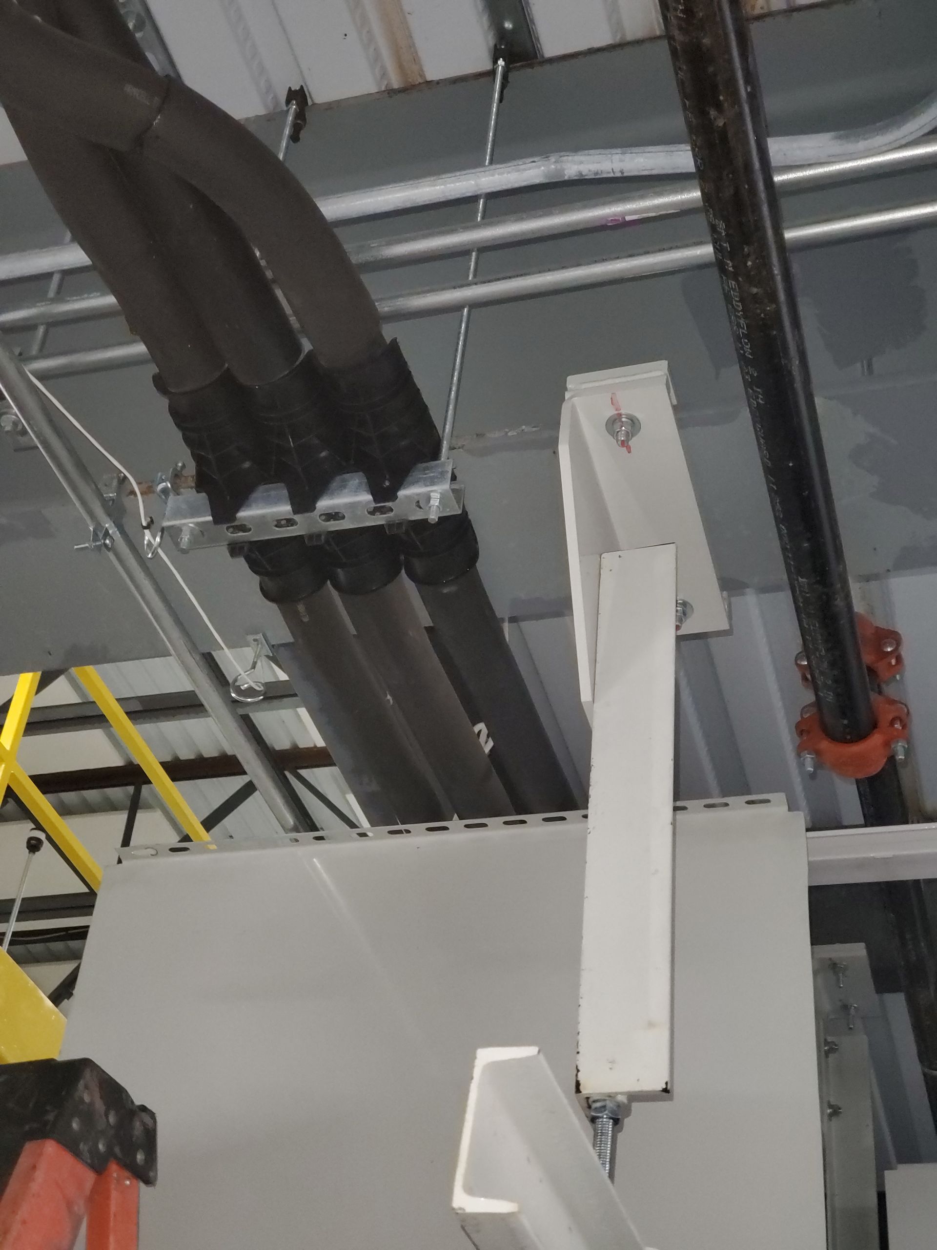Electrical conduits and pipes on a ceiling, with supporting brackets and metal framing.