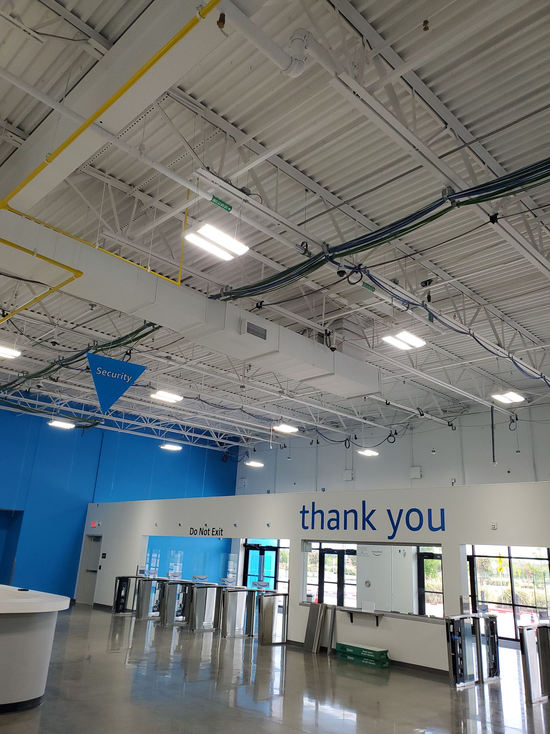 Interior of a brightly lit industrial building with white and blue walls, ceiling trusses, and turnstiles. The phrase 