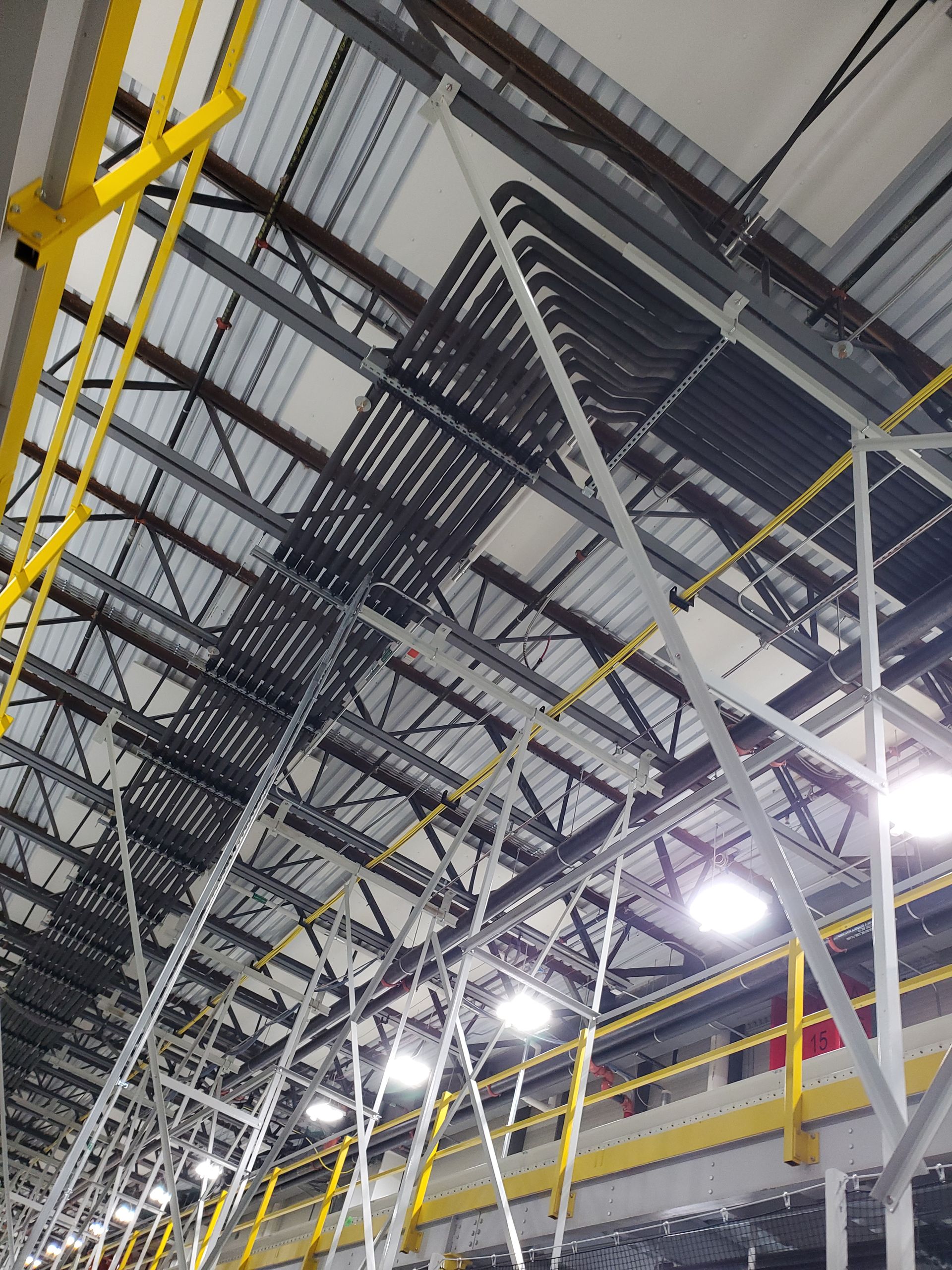 Overhead view of an industrial interior. Cables are run along the ceiling supports. Yellow handrails and metal framework.