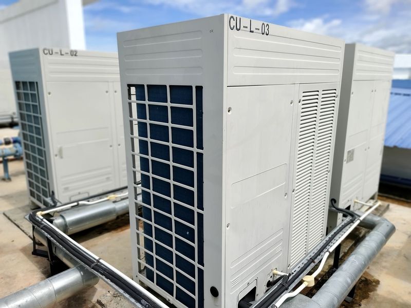 Outdoor HVAC condenser units with blue fan grilles and metal piping on a rooftop platform