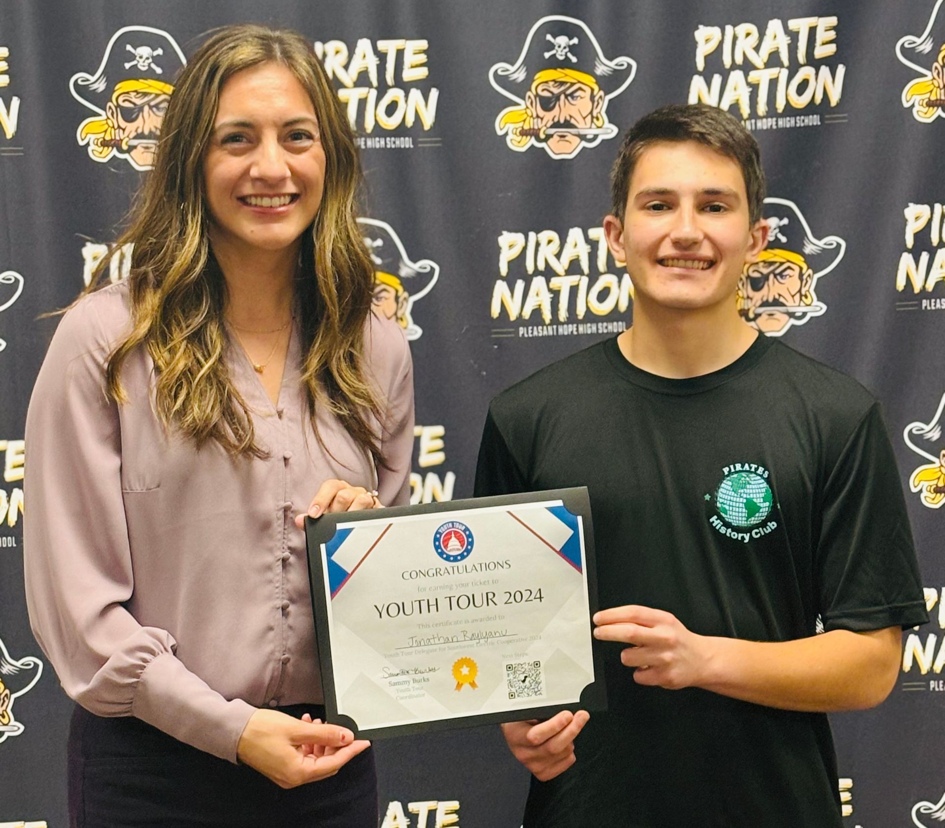 A man and a woman are holding a certificate in front of a pirate nation background