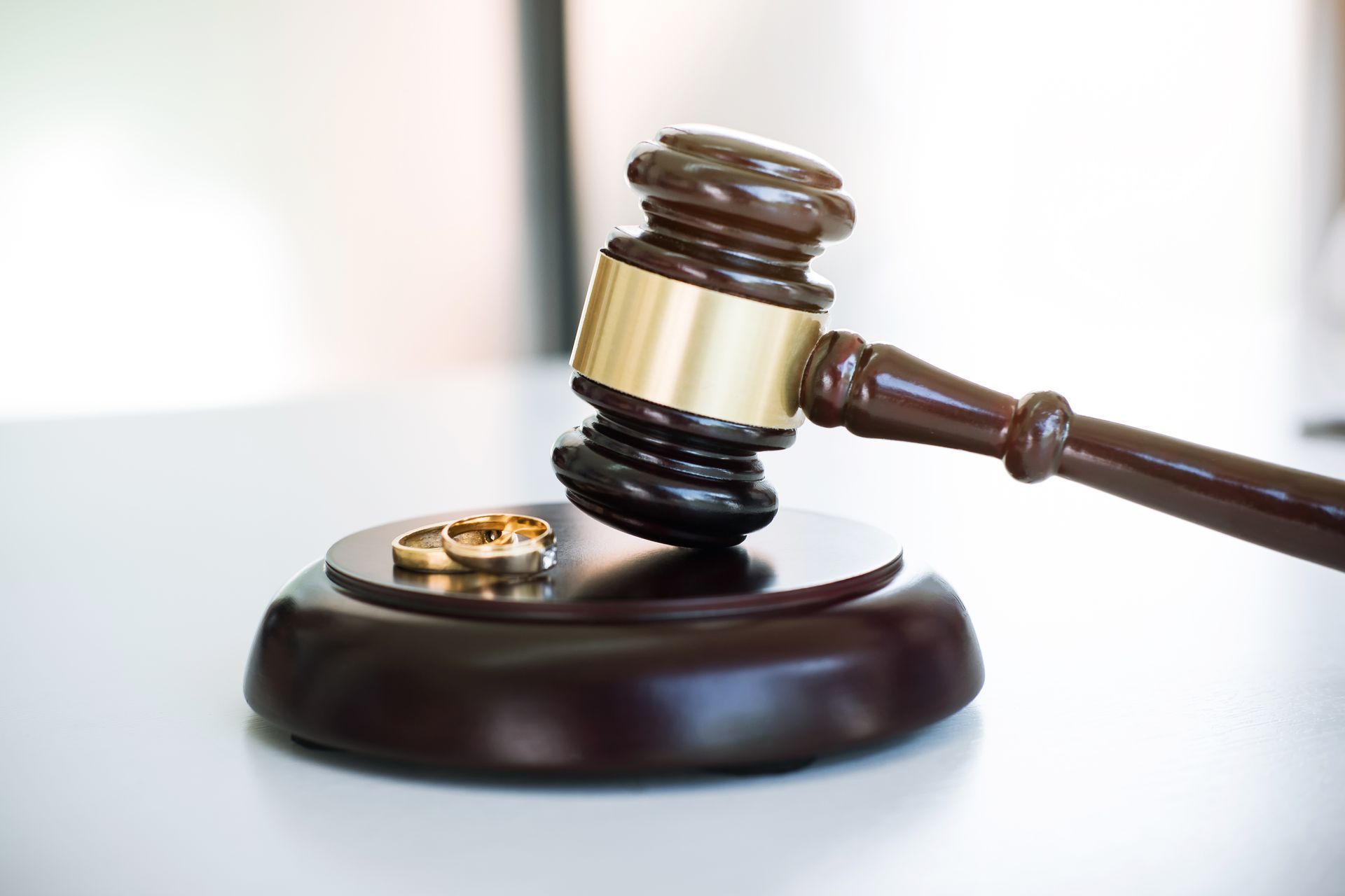 Gavel hitting a block next to two wedding rings, symbolizing a divorce in a court setting.