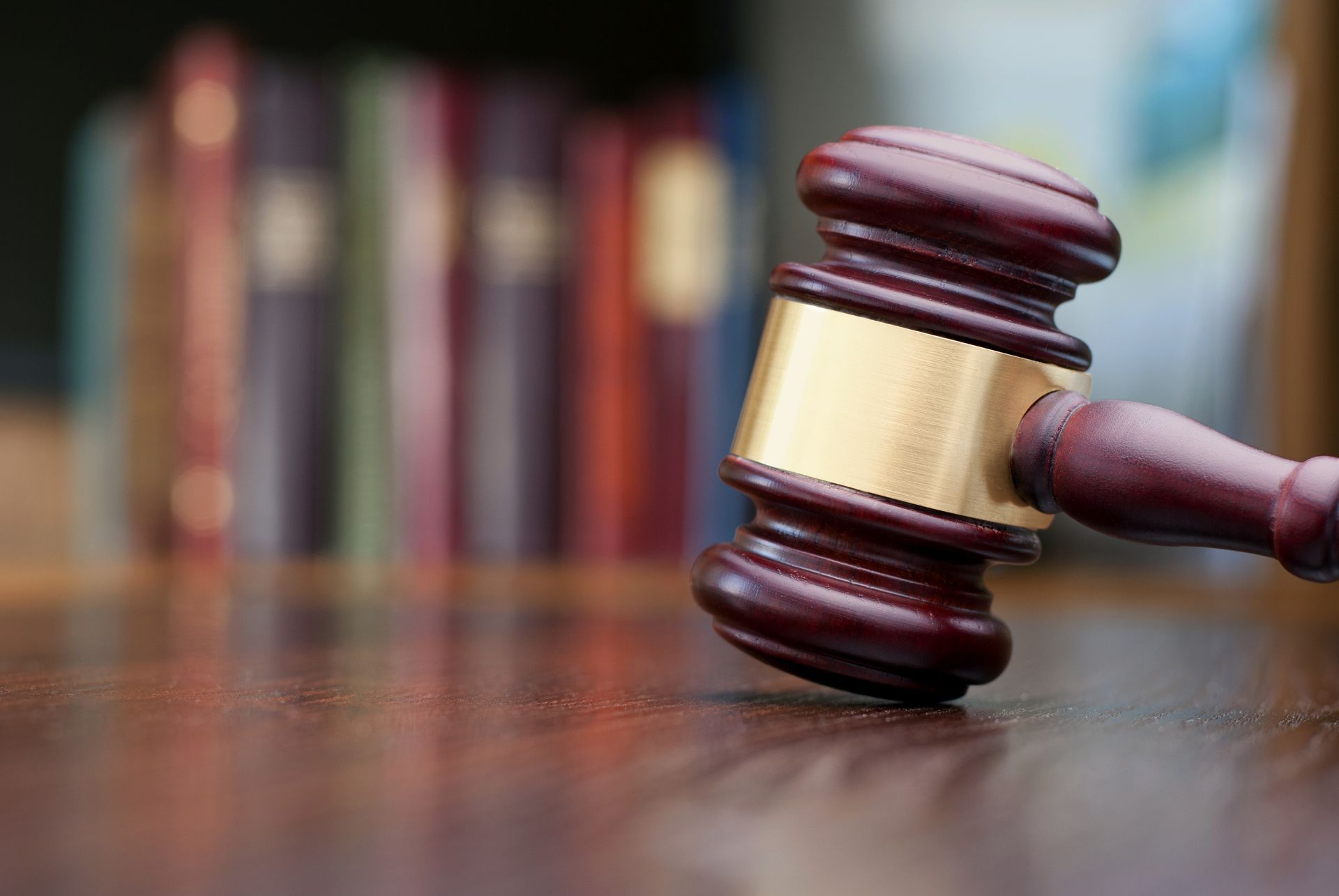 Wooden gavel on a brown table, with blurred bookshelves in the background.